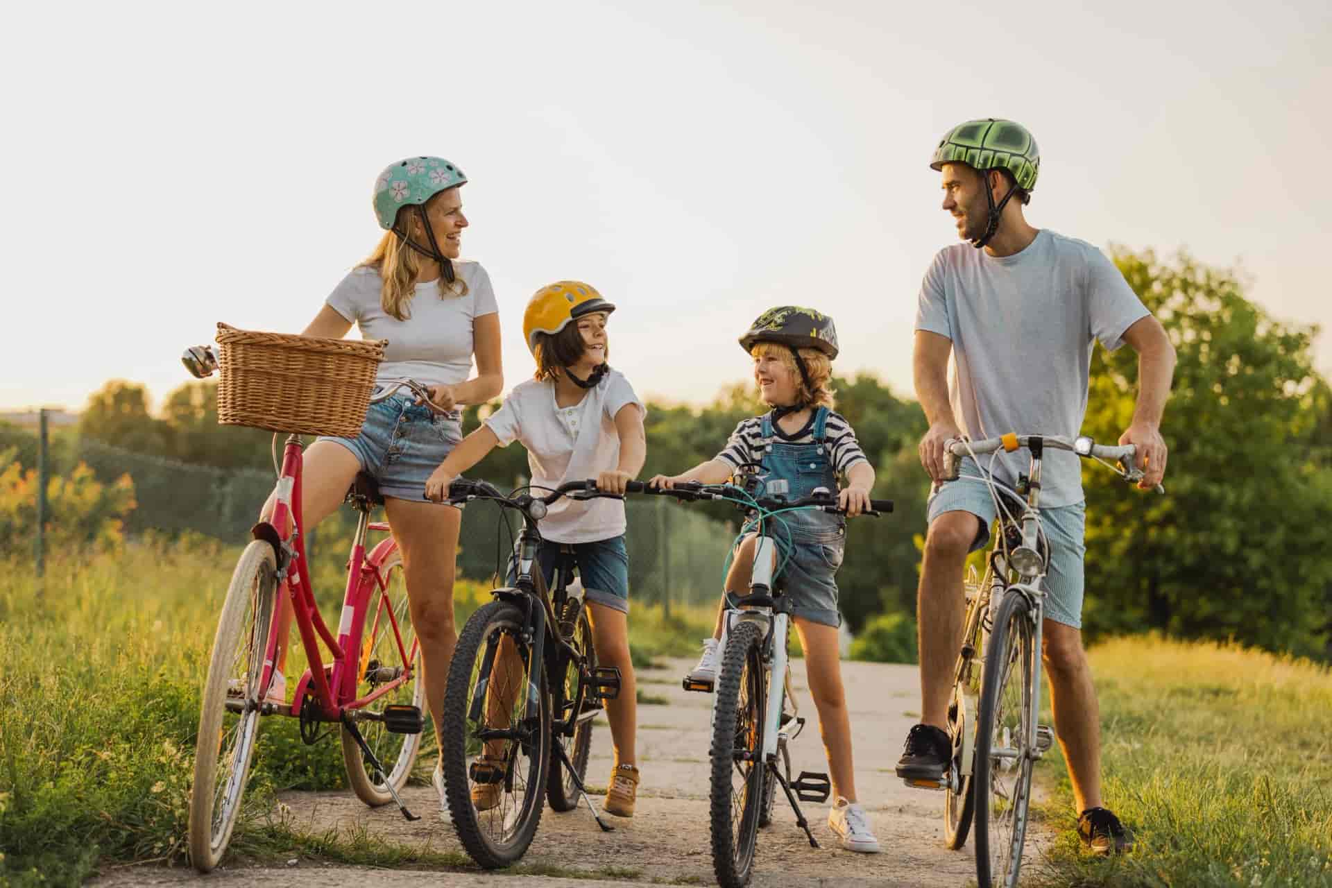 Family cycling outdoors on a sunny path with green grass and trees.
