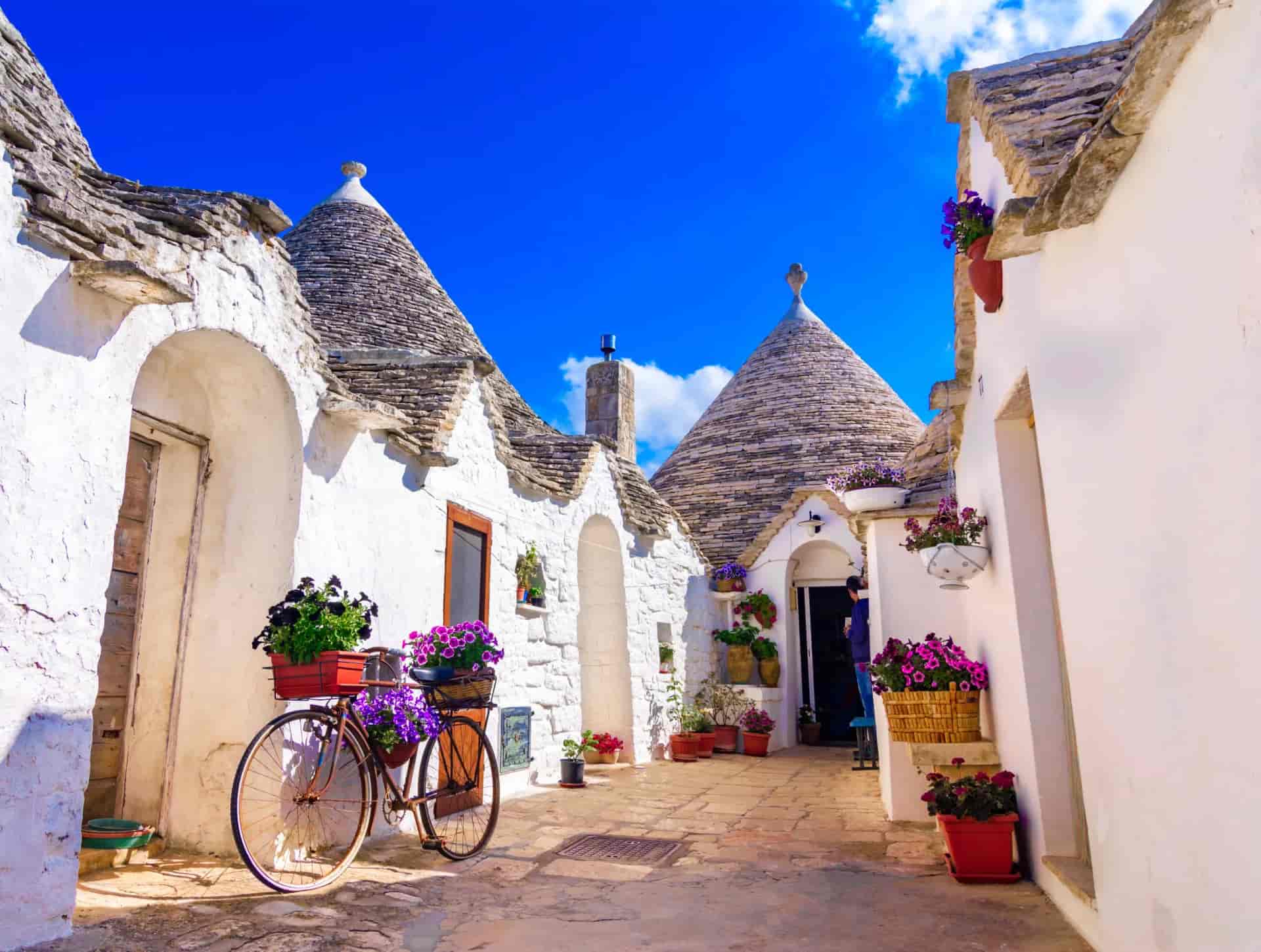 White trulli houses with conical stone roofs and bicycle decorated with purple flowers in Puglia.