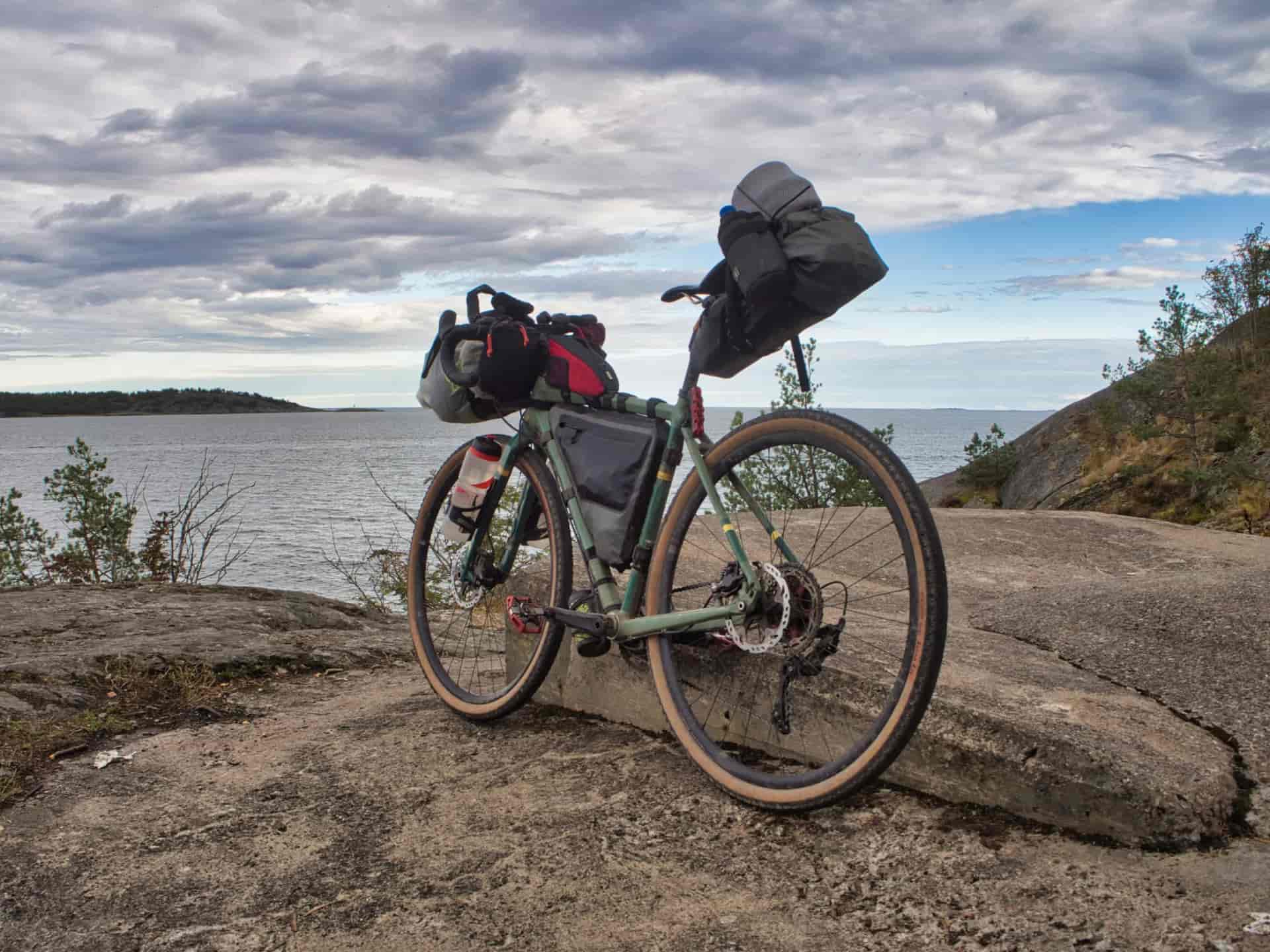 Bikepacking bicycle resting on rocky shore overlooking water under cloudy sky in Italy