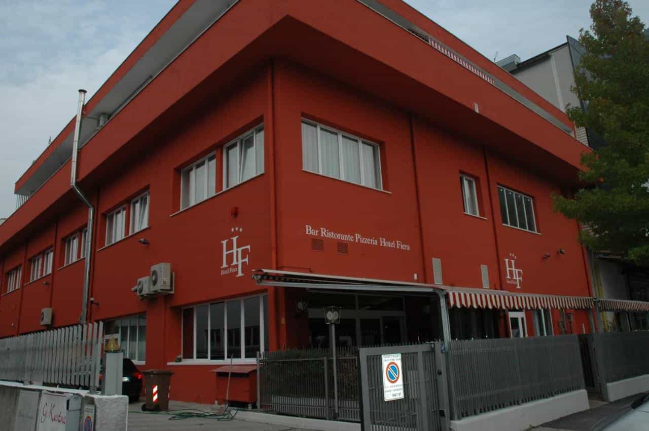Red exterior Hotel Ristorante Pizzeria Hotel Fiera building with white lettering and gray fence.