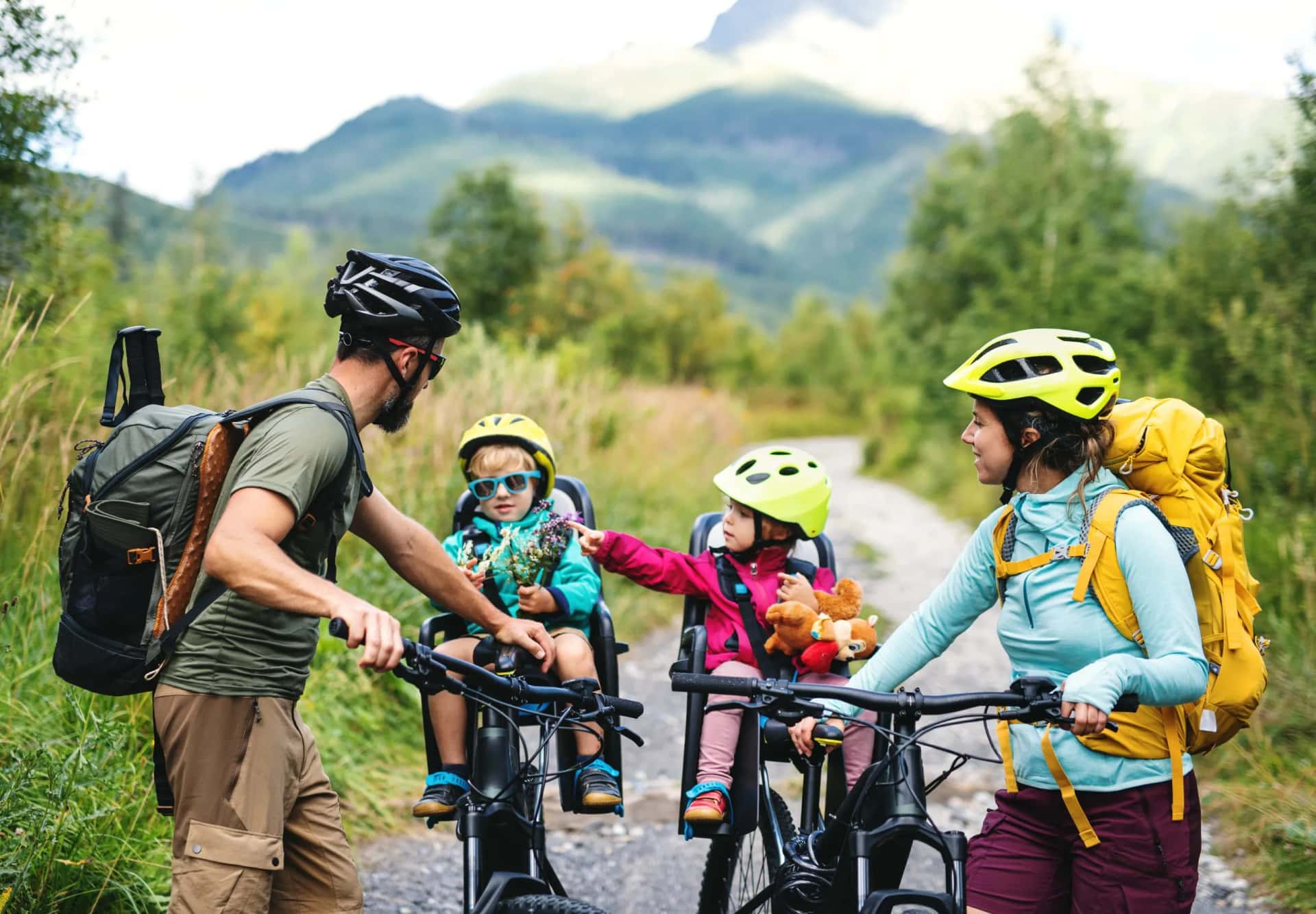 Family cycling with children in bike seats on a dirt path with mountains in the background.