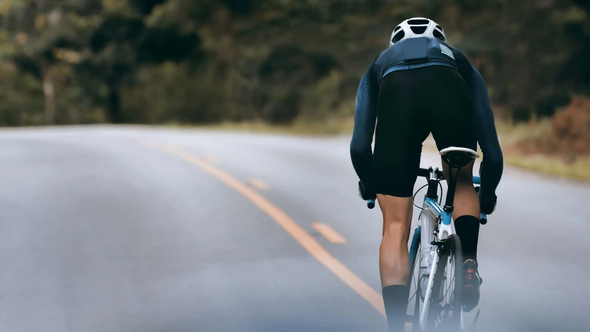 Cyclist in helmet riding on paved road through forested area in Italy