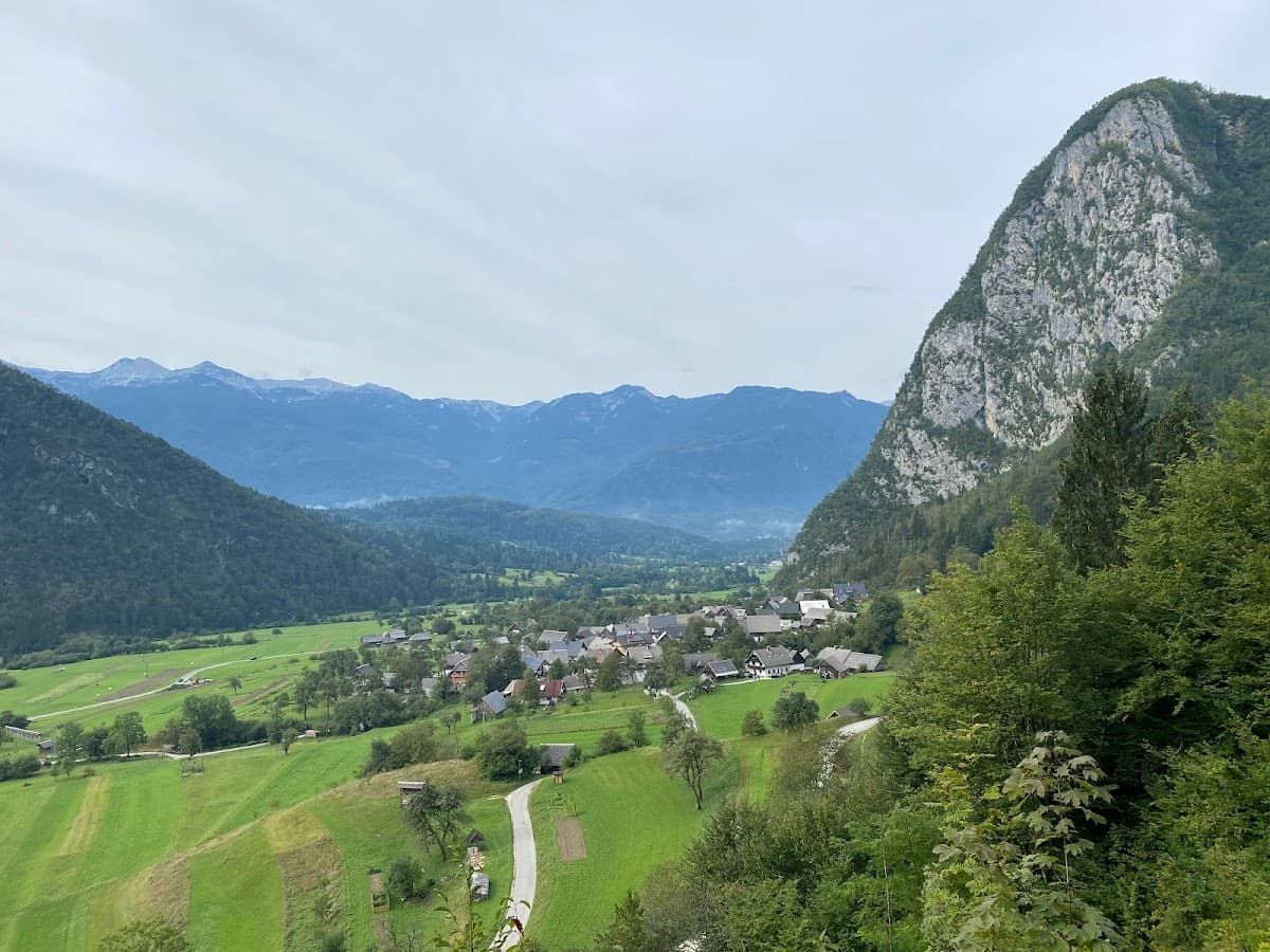 Alpine village nestled in a green valley surrounded by steep, forested mountains under a cloudy sky.