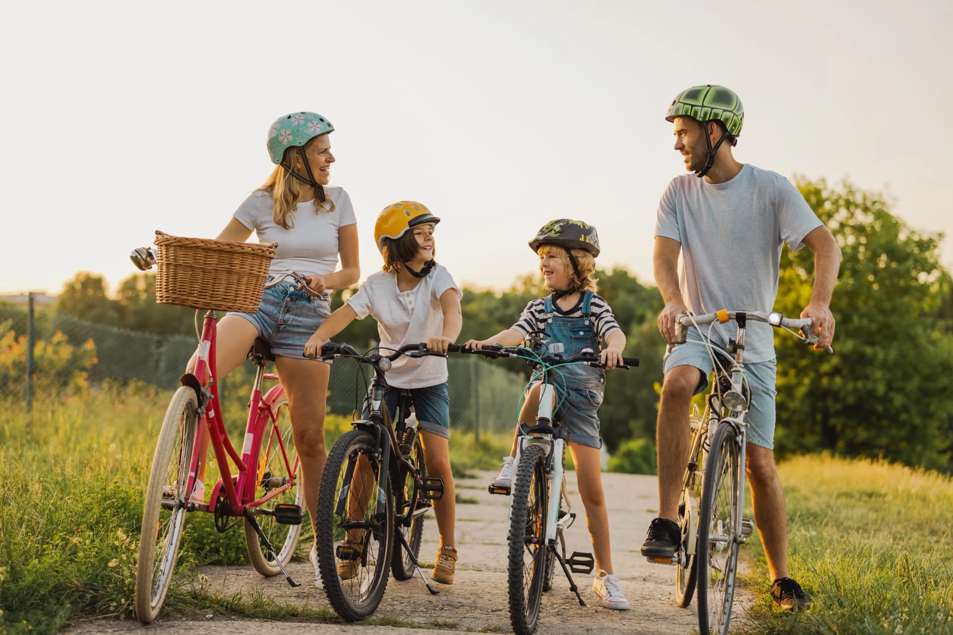 Family cycling outdoors on a sunny path with green grass and trees.