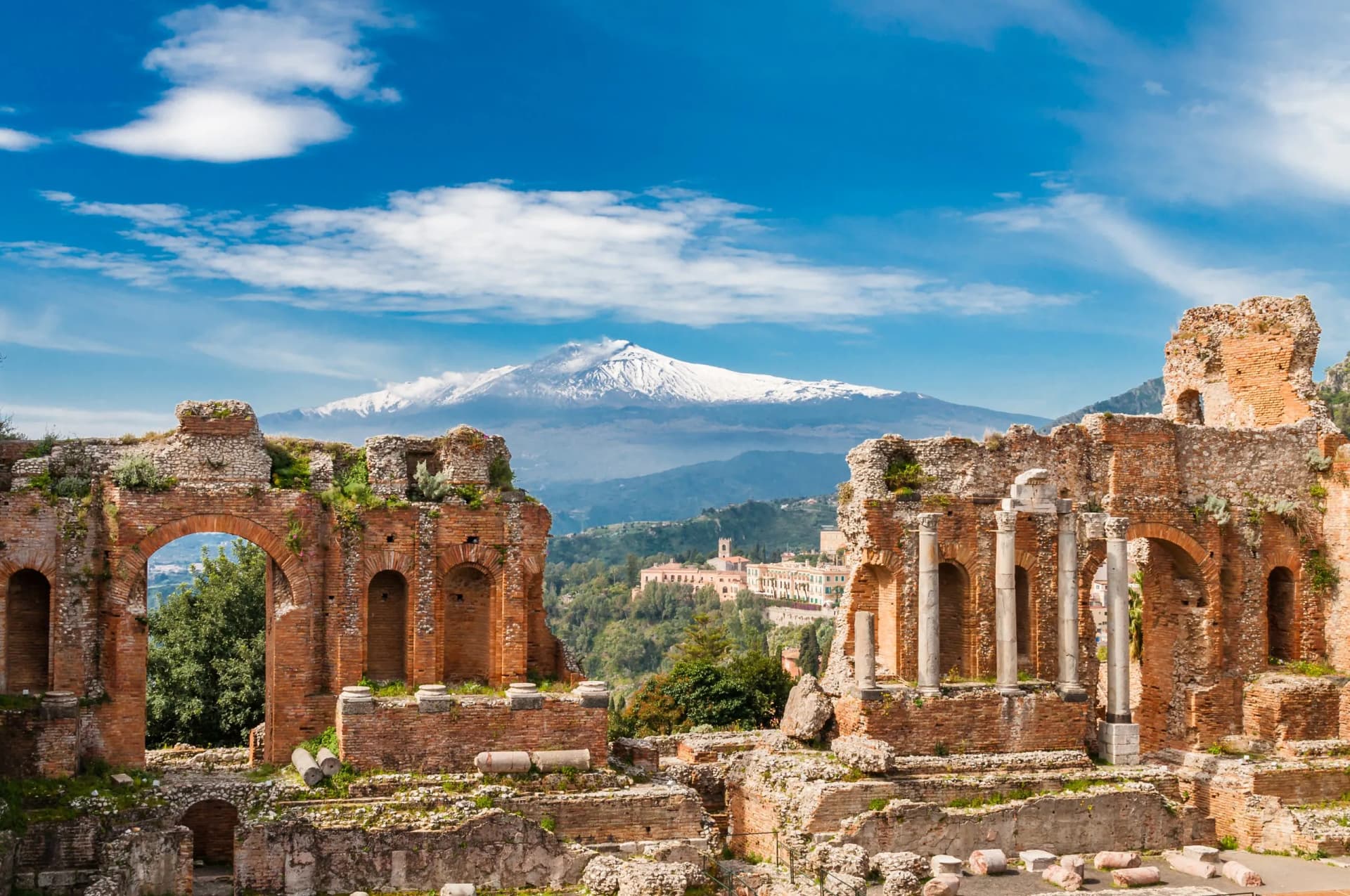 Ancient Roman theater ruins with snow-capped Mount Etna in Sicily background.