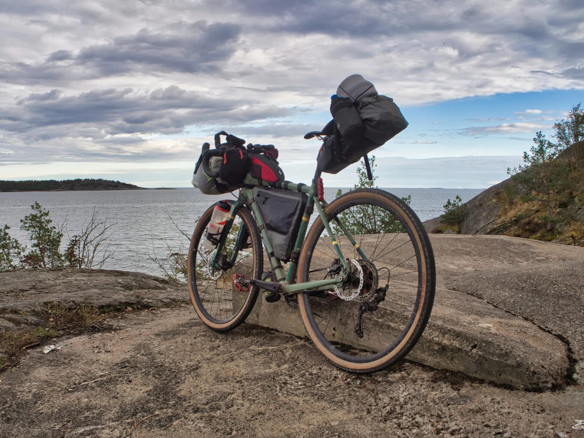 Bikepacking bicycle resting on rocky shore overlooking water under cloudy sky in Italy