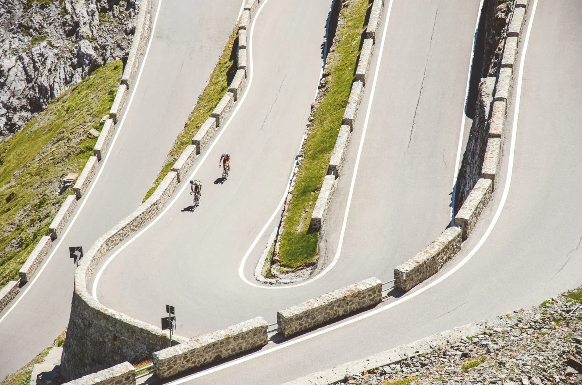 Cyclists ascending steep switchbacks on a mountain pass road with stone barriers, Stelvio.