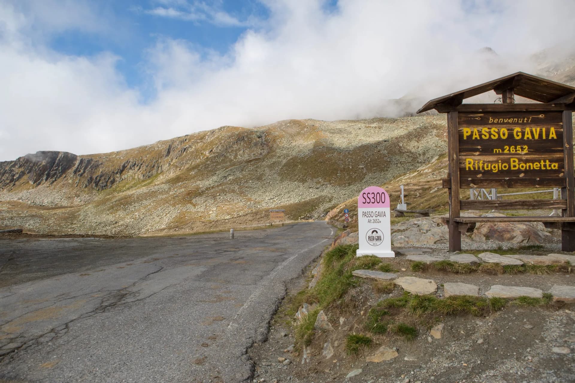 Passo Gavia welcome sign at 2652m altitude with rocky mountain landscape and clouds.