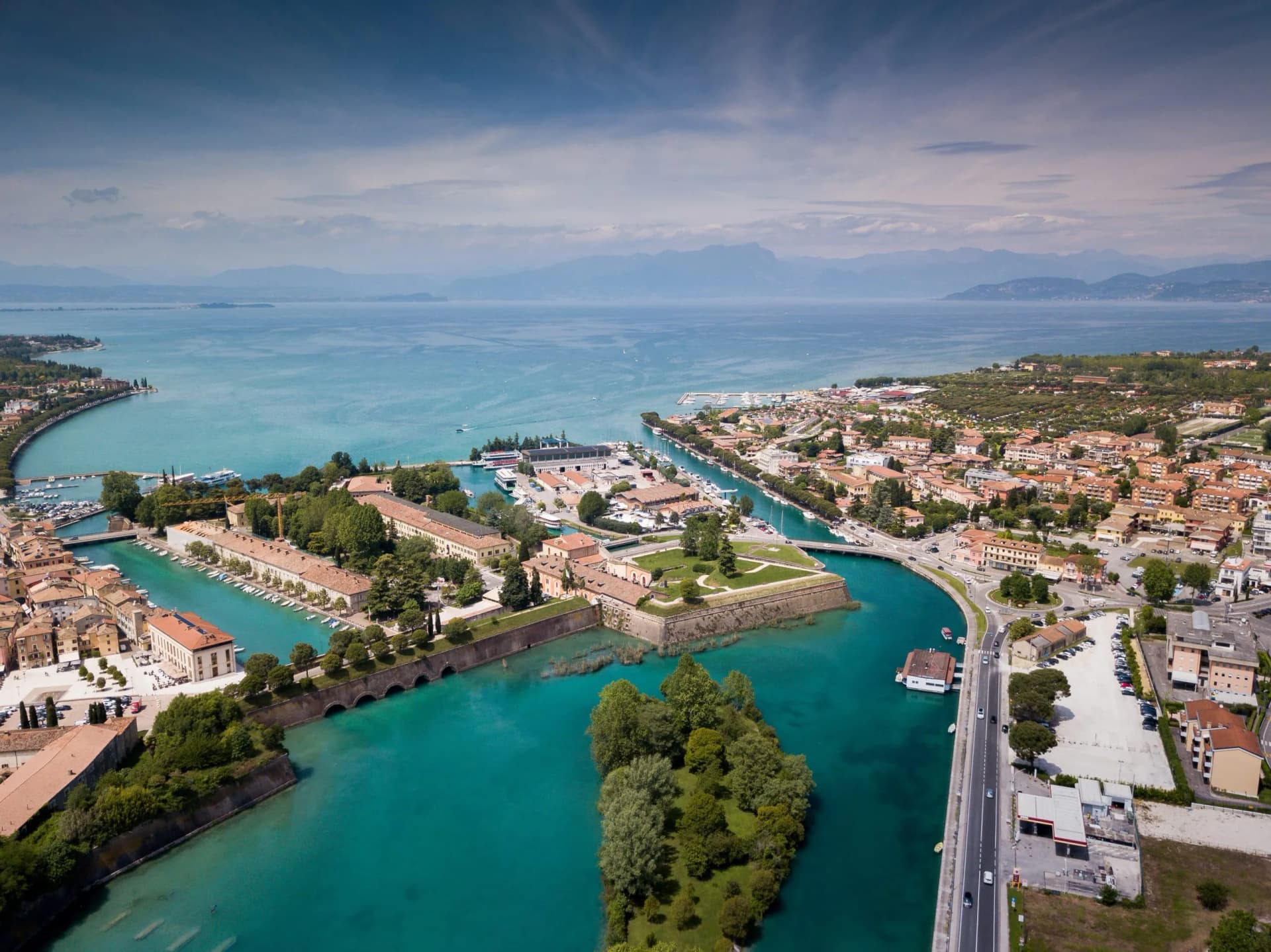 Aerial view of Peschiera del Garda town with turquoise canals, harbor, and Lake Garda in the background.