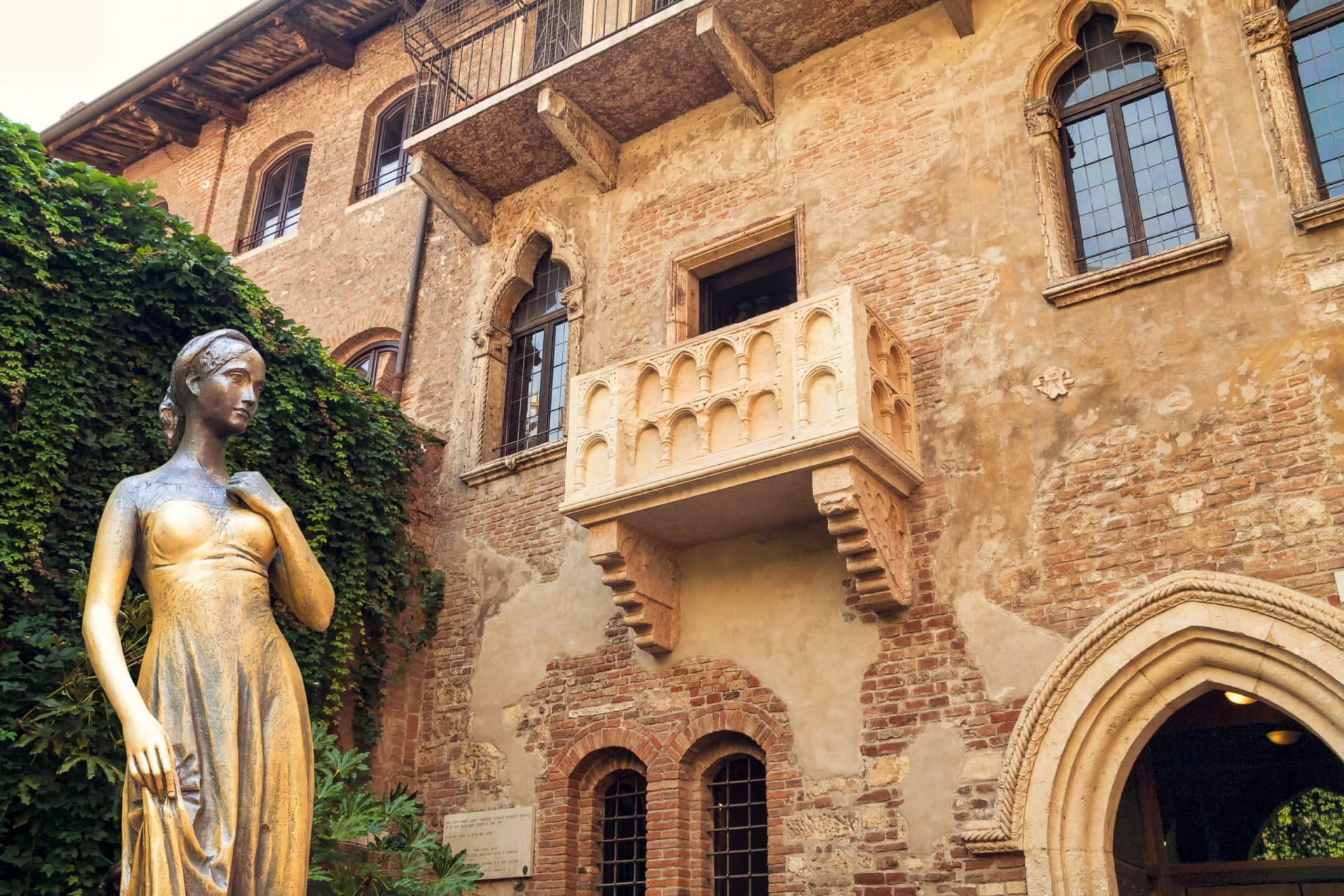 Statue of Juliet in front of historic brick building with balcony in Verona.