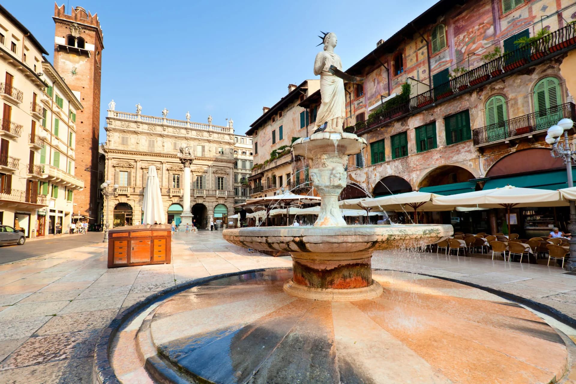 Fountain statue in Piazza delle Erbe with historic buildings and outdoor cafe seating in Verona.