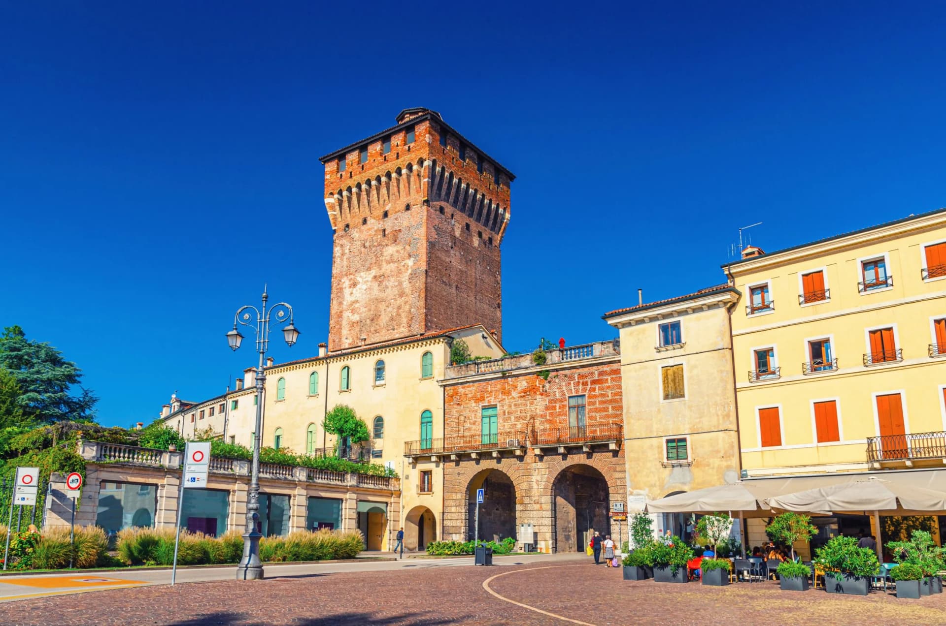 Historic brick tower next to colorful buildings with outdoor cafe seating in Vicenza.