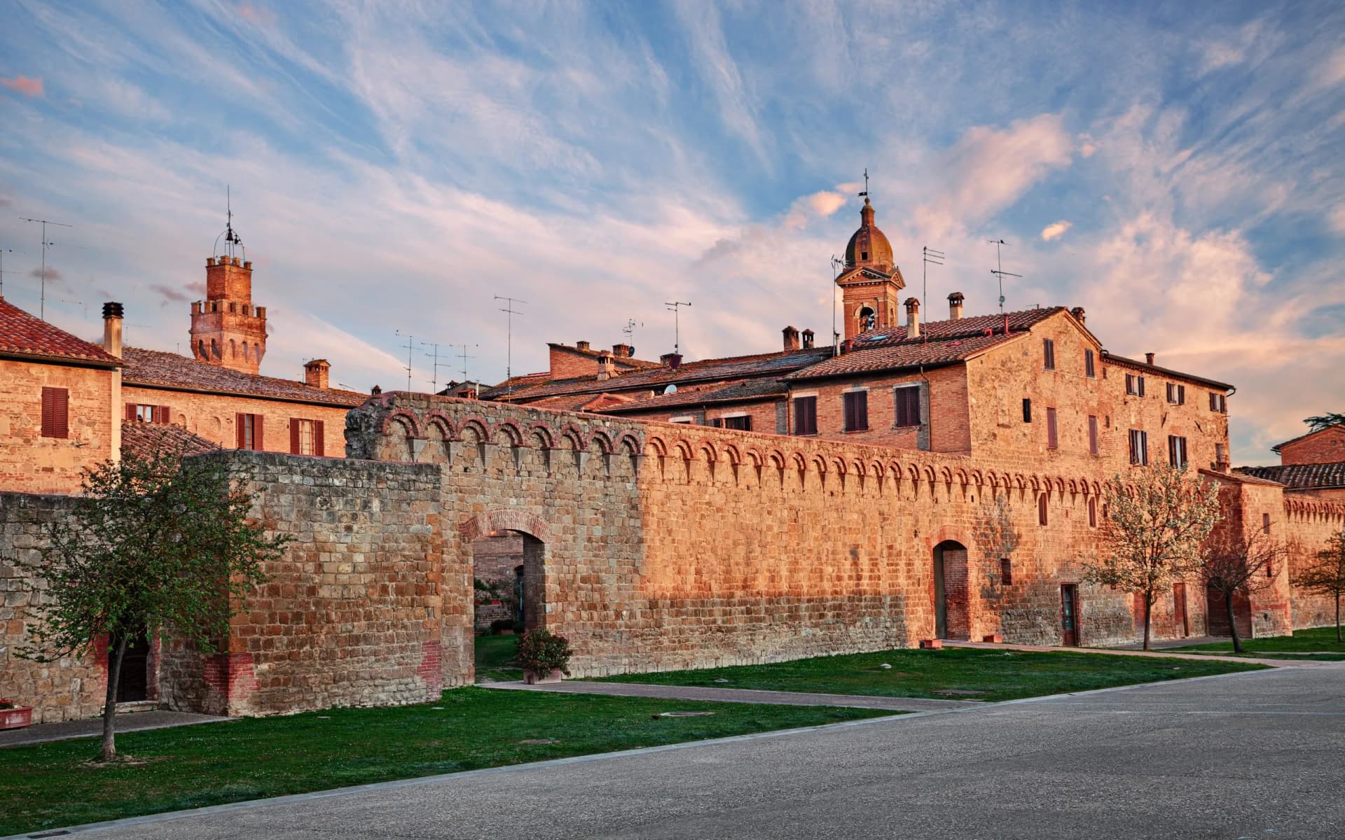 Historic stone wall and brick buildings in Buonconvento under a dramatic sunset sky.