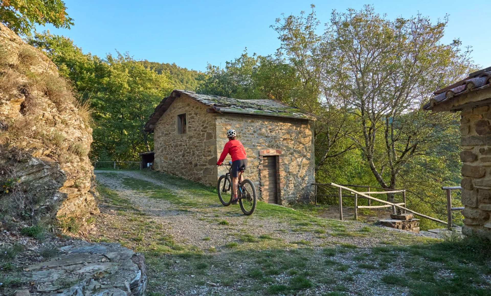 Mountain biking past a stone hut on a gravel path in Tuscany.