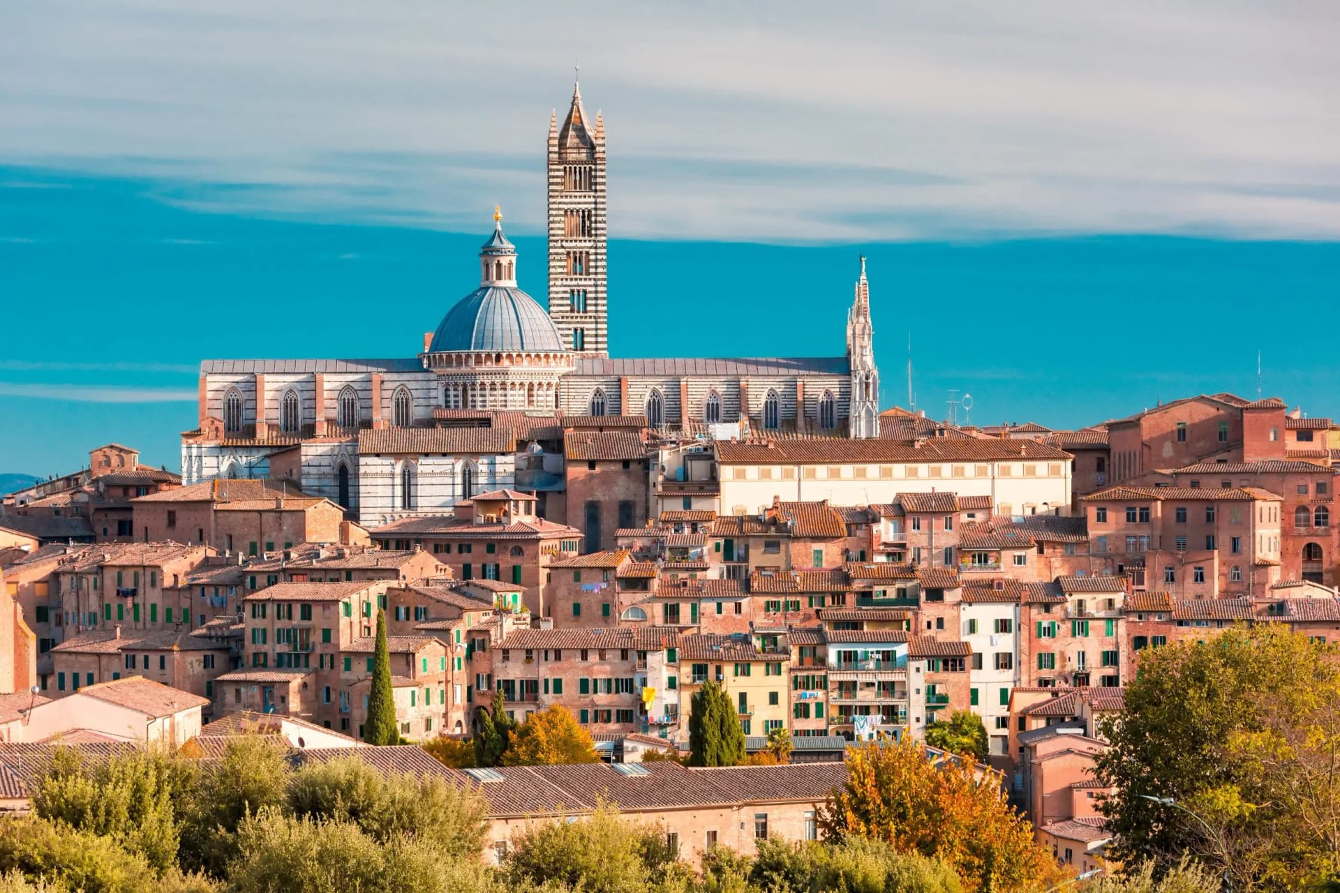 Siena cityscape with Duomo cathedral dome and striped bell tower under bright blue sky