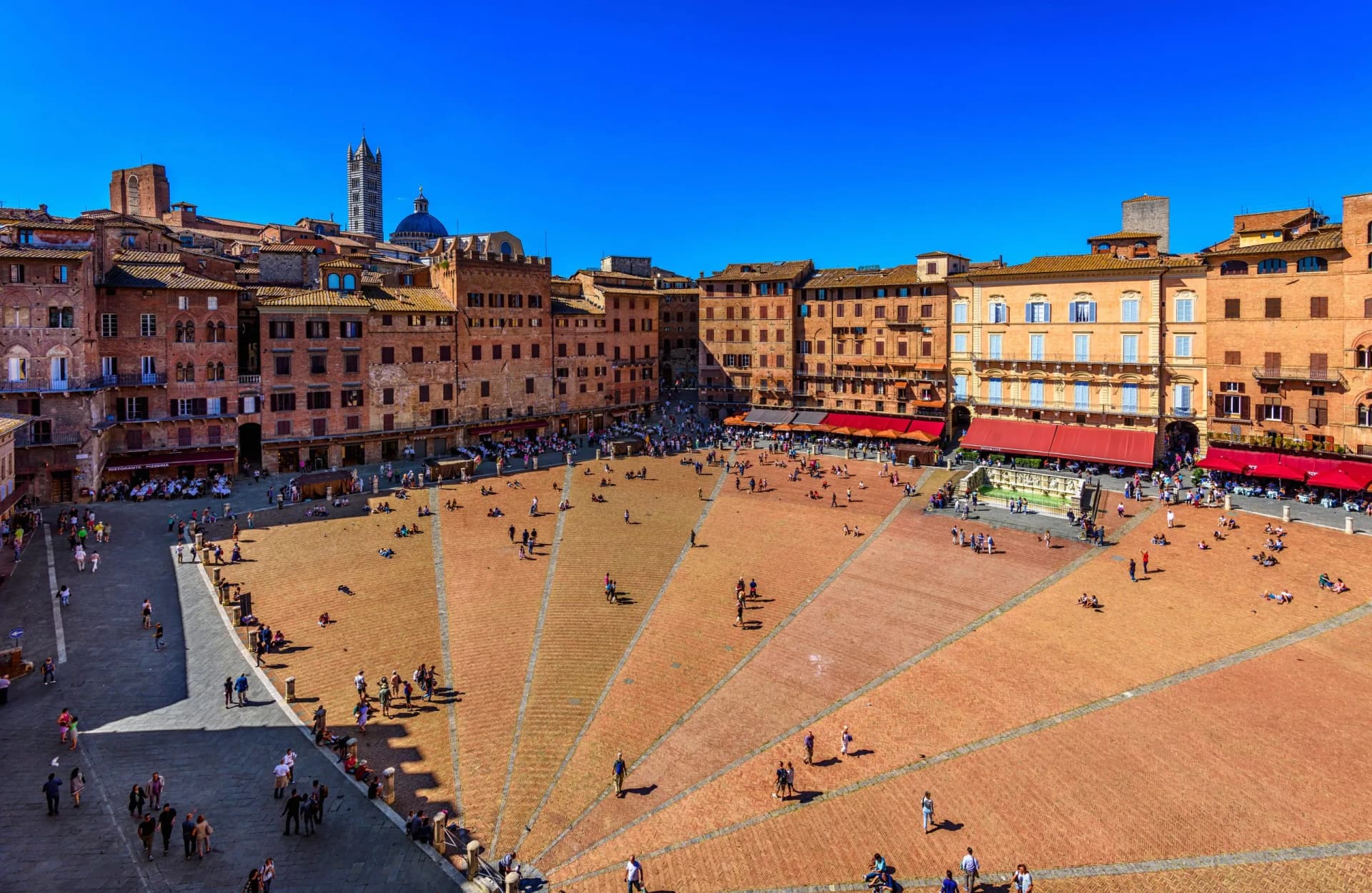Piazza del Campo square with people relaxing under a bright blue sky in Siena, Italy.