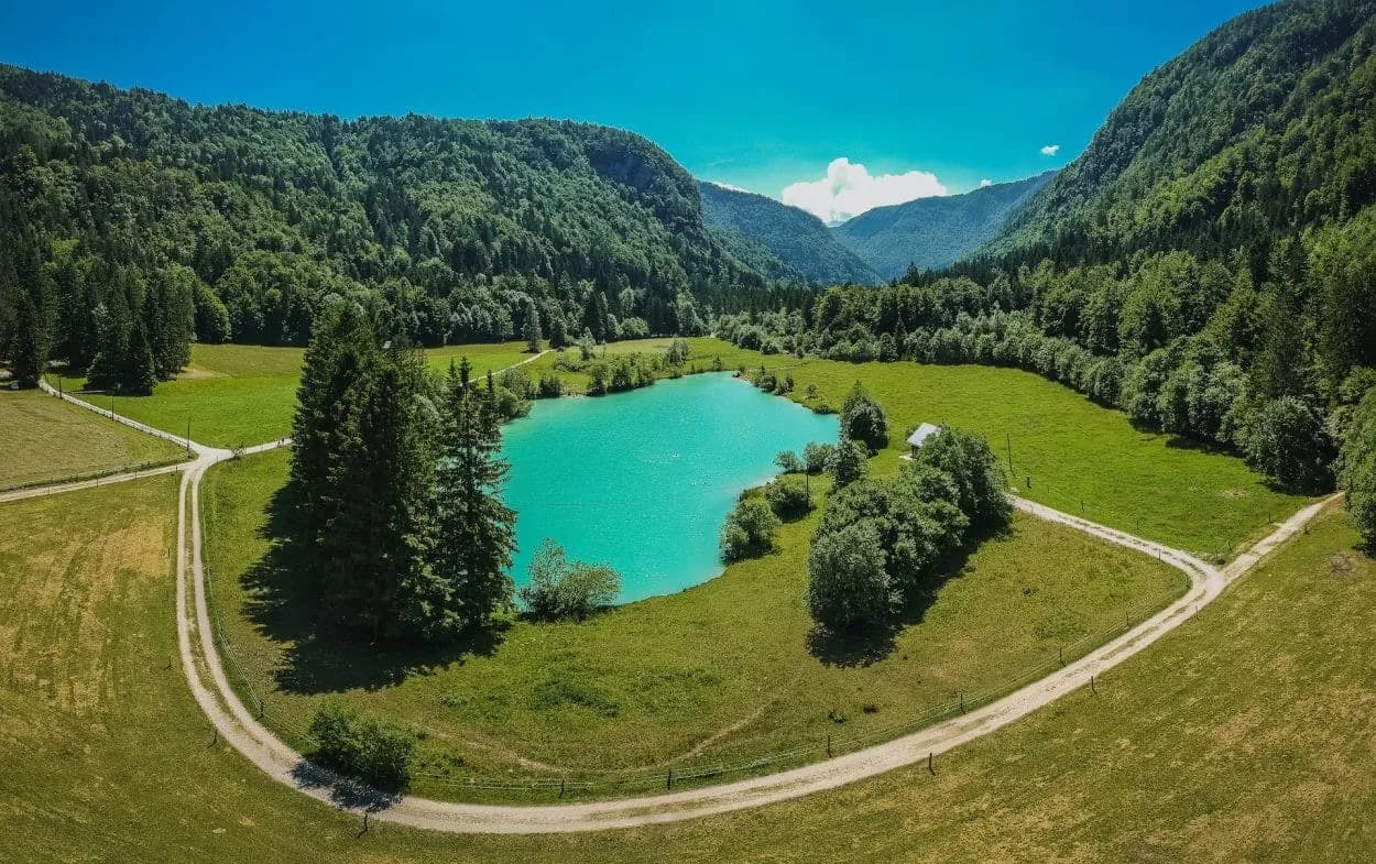 Turquoise mountain lake surrounded by green forests and meadows under a clear blue sky at Lake Kreda