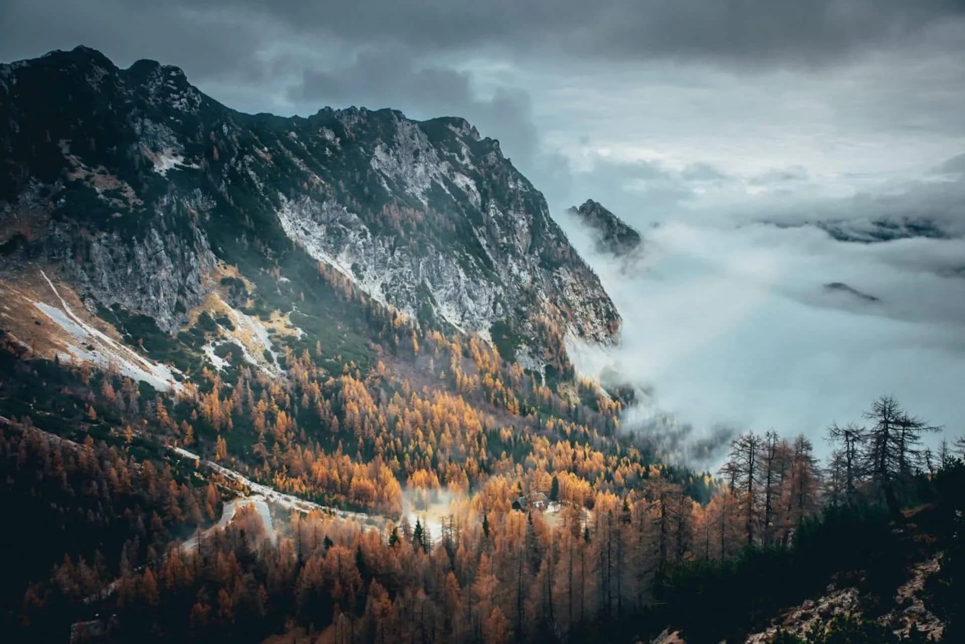 Winding road through mountains with autumn forest and low clouds near Vršič Pass, Slovenia.