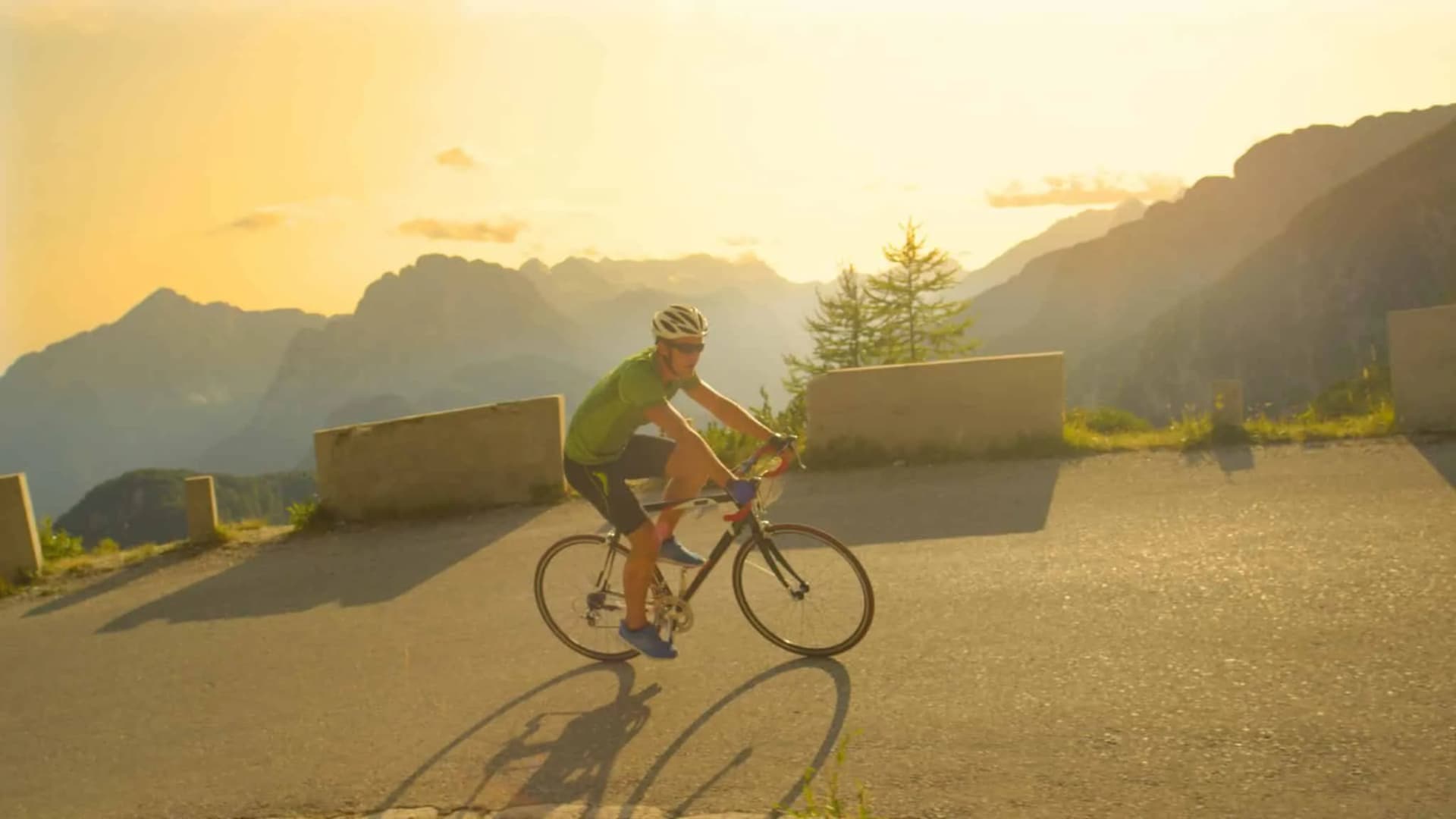 Road cycling up Vršič Pass with dramatic mountain backdrop at sunset