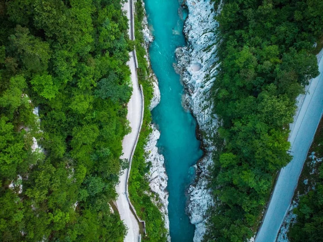 Aerial view of bright turquoise river canyon with roads winding through dense green forest.