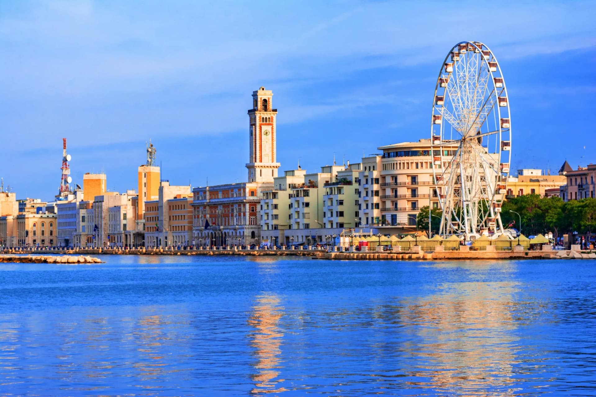 Bari waterfront skyline with Ferris wheel and clock tower reflected in blue water