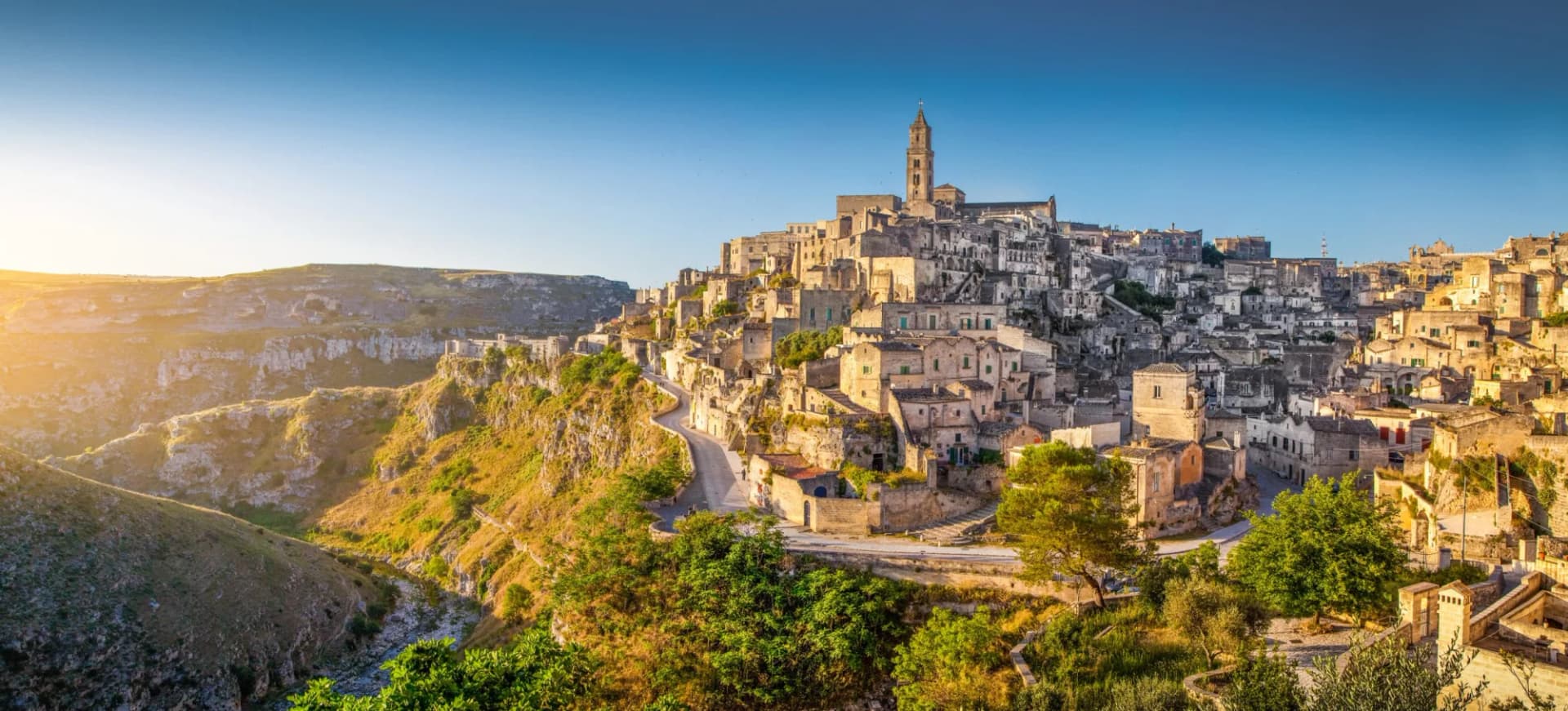 Historic stone city built into a ravine hillside with a prominent bell tower, Matera