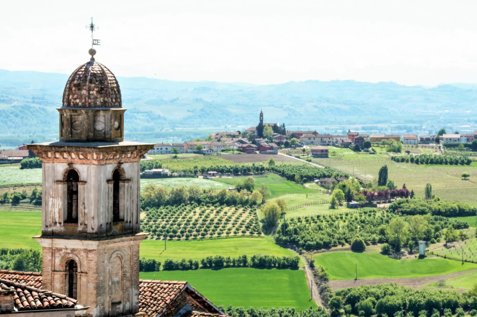 Bell tower dome overlooking green rolling hills and village in the Langhe landscape.