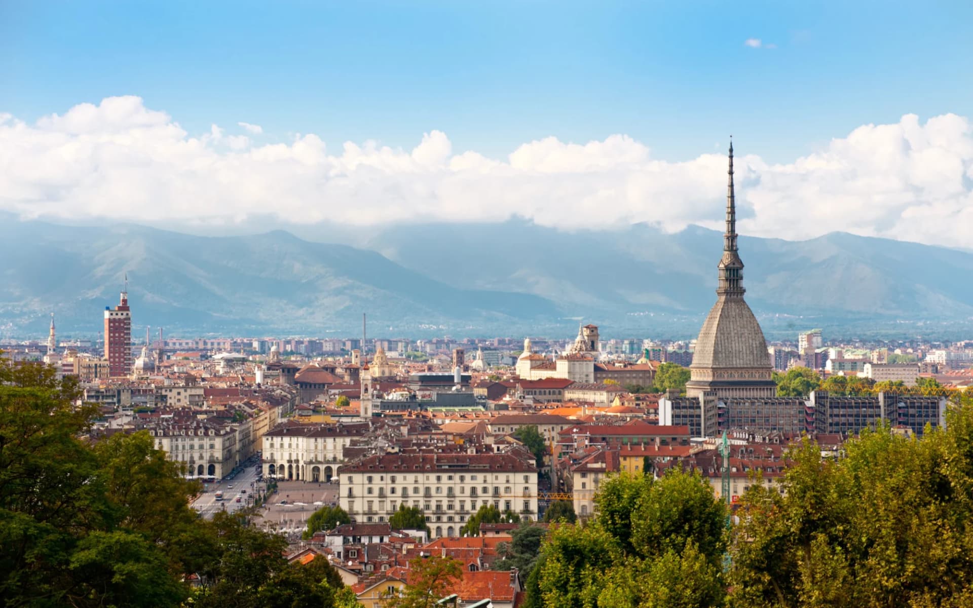 Cityscape of Turin with Mole Antonelliana and Alps under a blue sky with clouds.