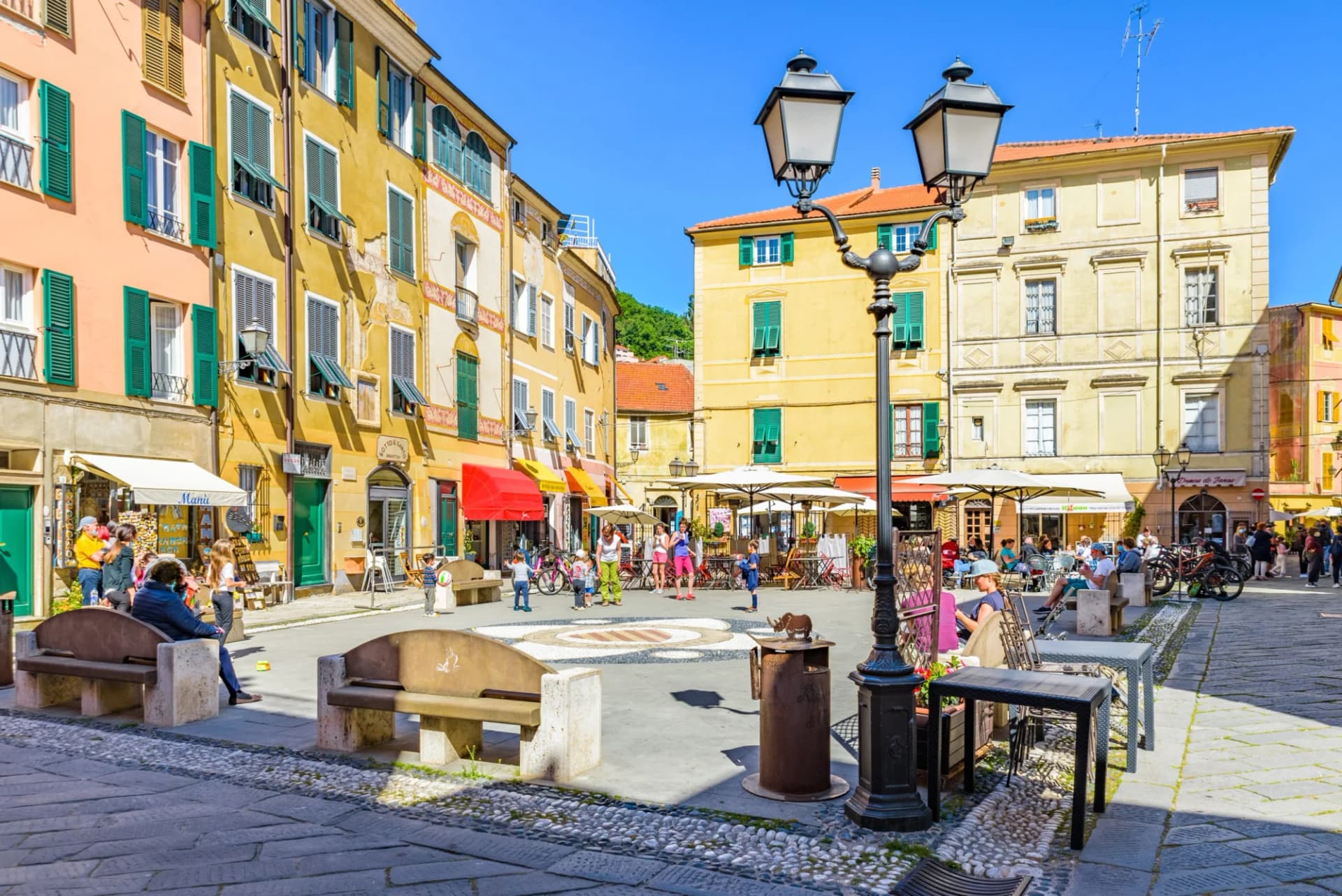 Piazza Garibaldi in Finale Ligure with colorful buildings, outdoor cafe seating, and people relaxing.