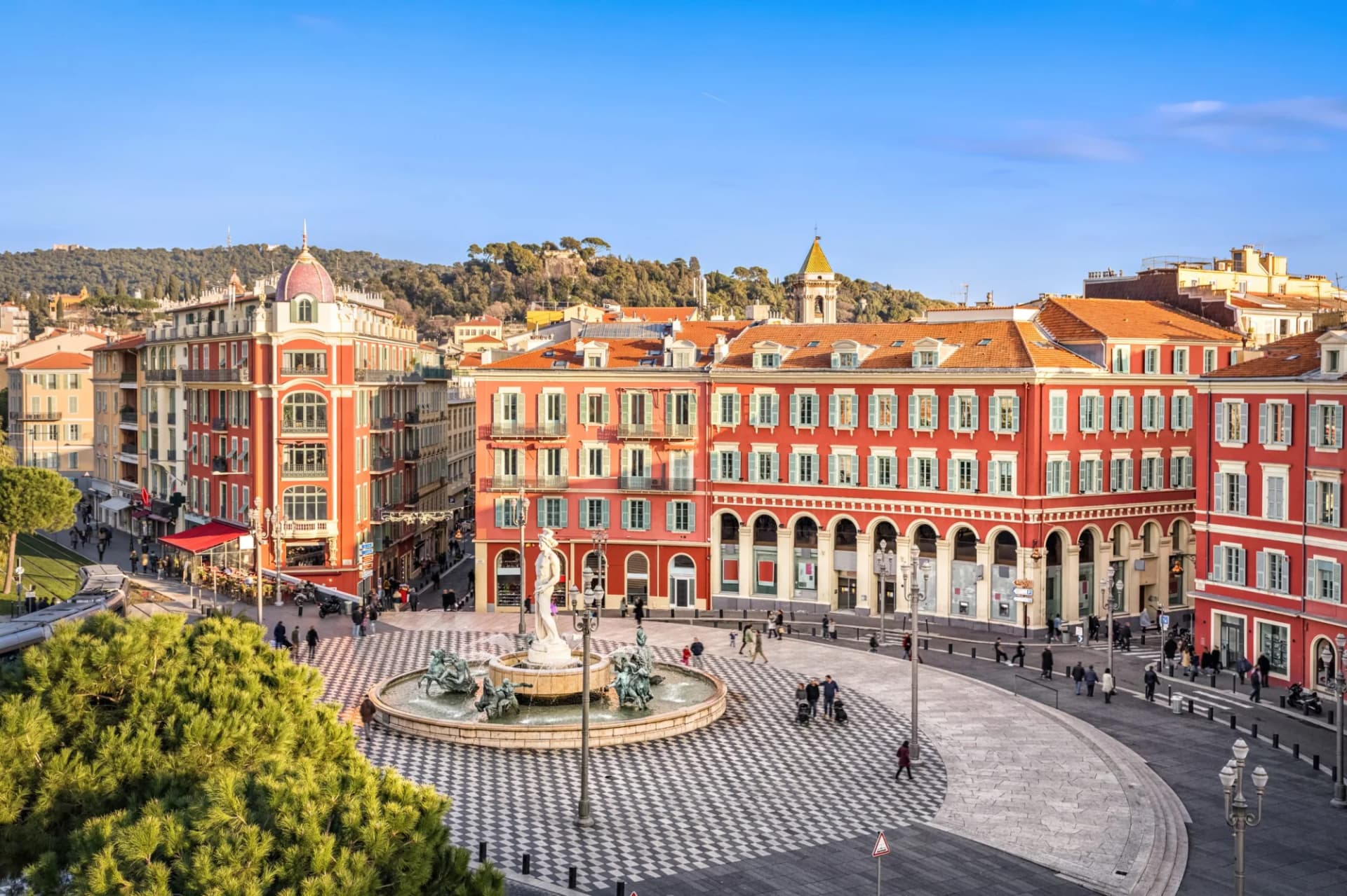 Fountain in Place Masséna square with red buildings and green hills in Nice