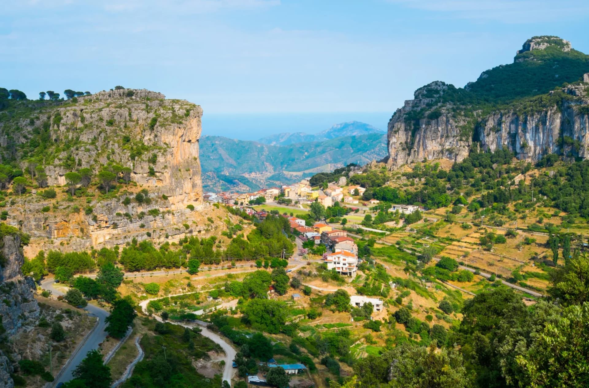 Village nestled between steep rocky cliffs overlooking distant mountains and the sea.
