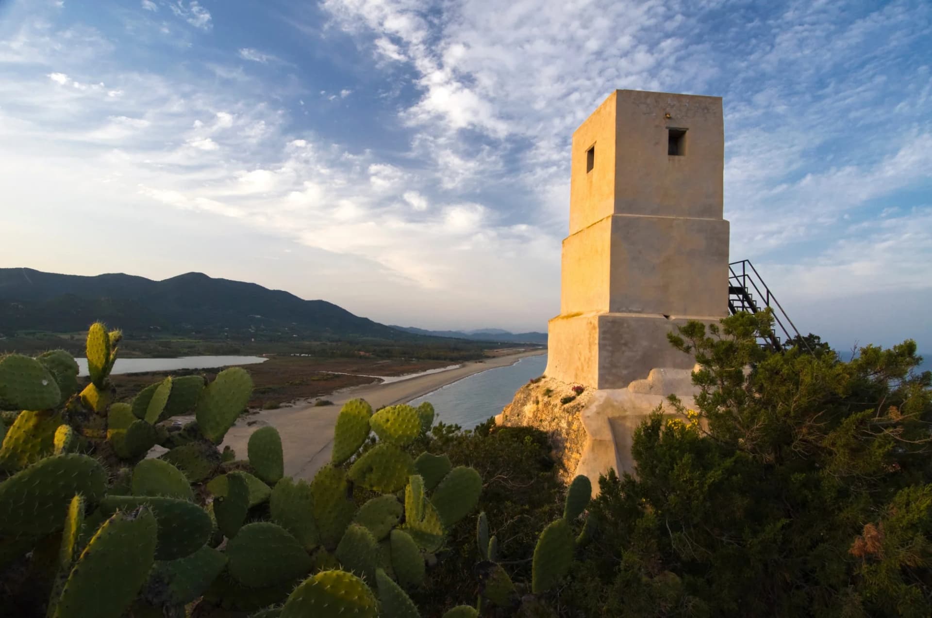 Stone watchtower overlooking a Mediterranean coastline with prickly pear cactus in the foreground.