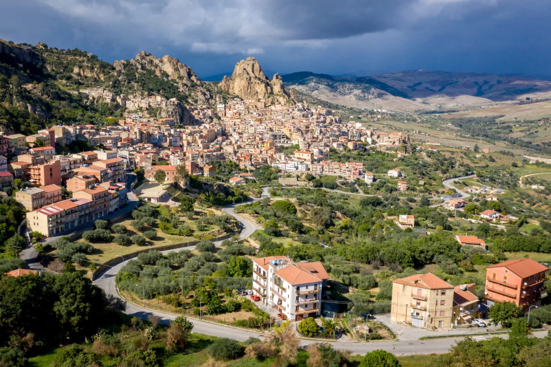Aerial view of Gagliano Castelferrato town nestled against rocky hills under dramatic sky in Sicily.