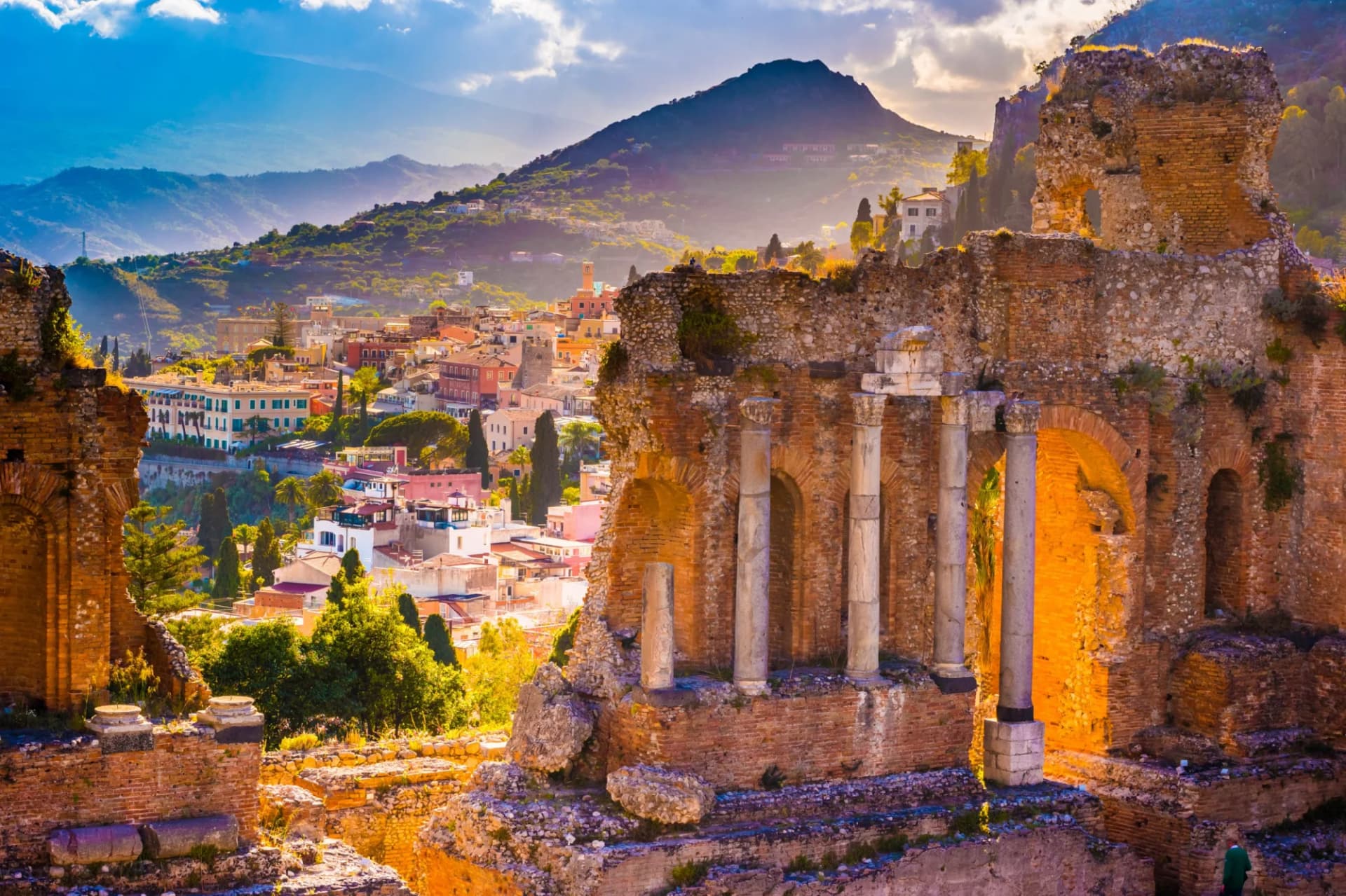 Ruins of the Ancient Theatre of Taormina at sunset overlooking the town and mountains.