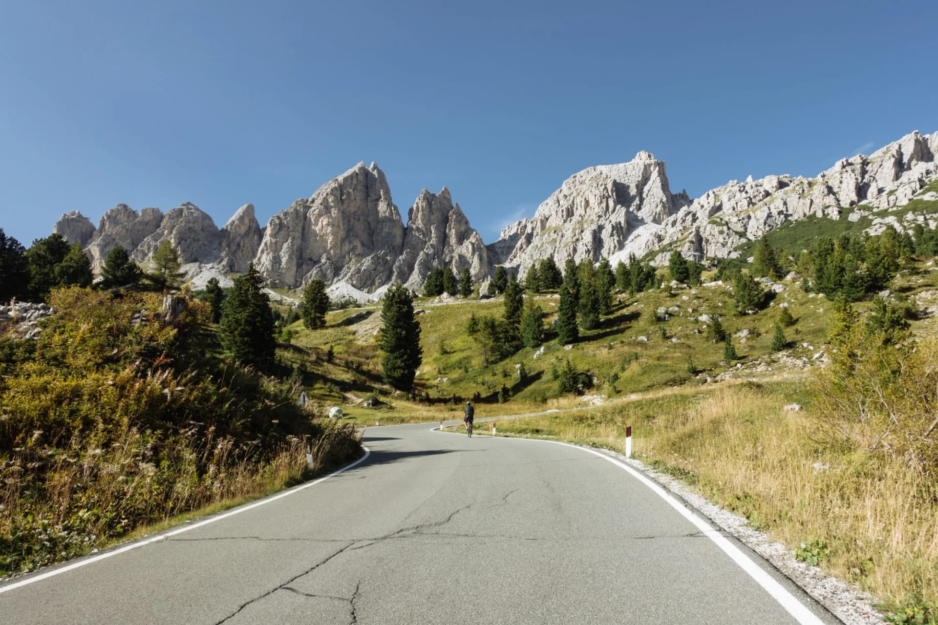 Cyclist on winding mountain road in the Italian Dolomites with rugged peaks.