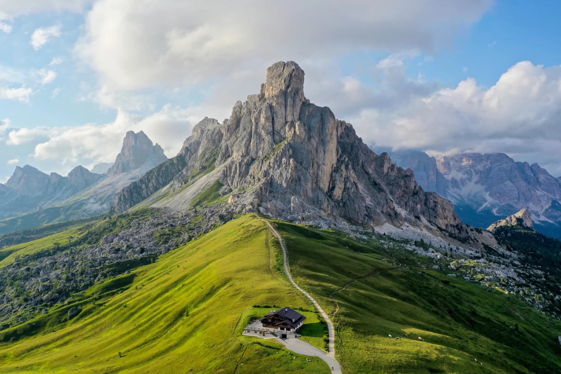 Mountain hut below jagged peaks on green ridge, Passo Giau, Dolomites, Italy.