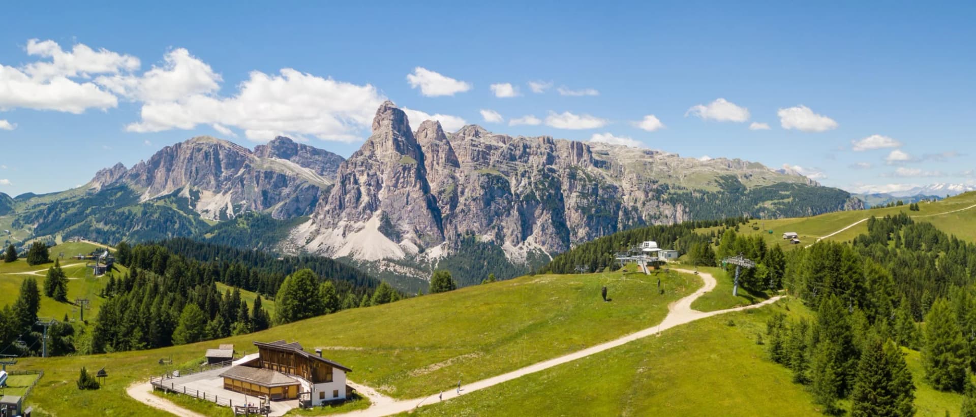 Great landscape on the Dolomites with rocky peaks, green meadows, and a ski lift station.
