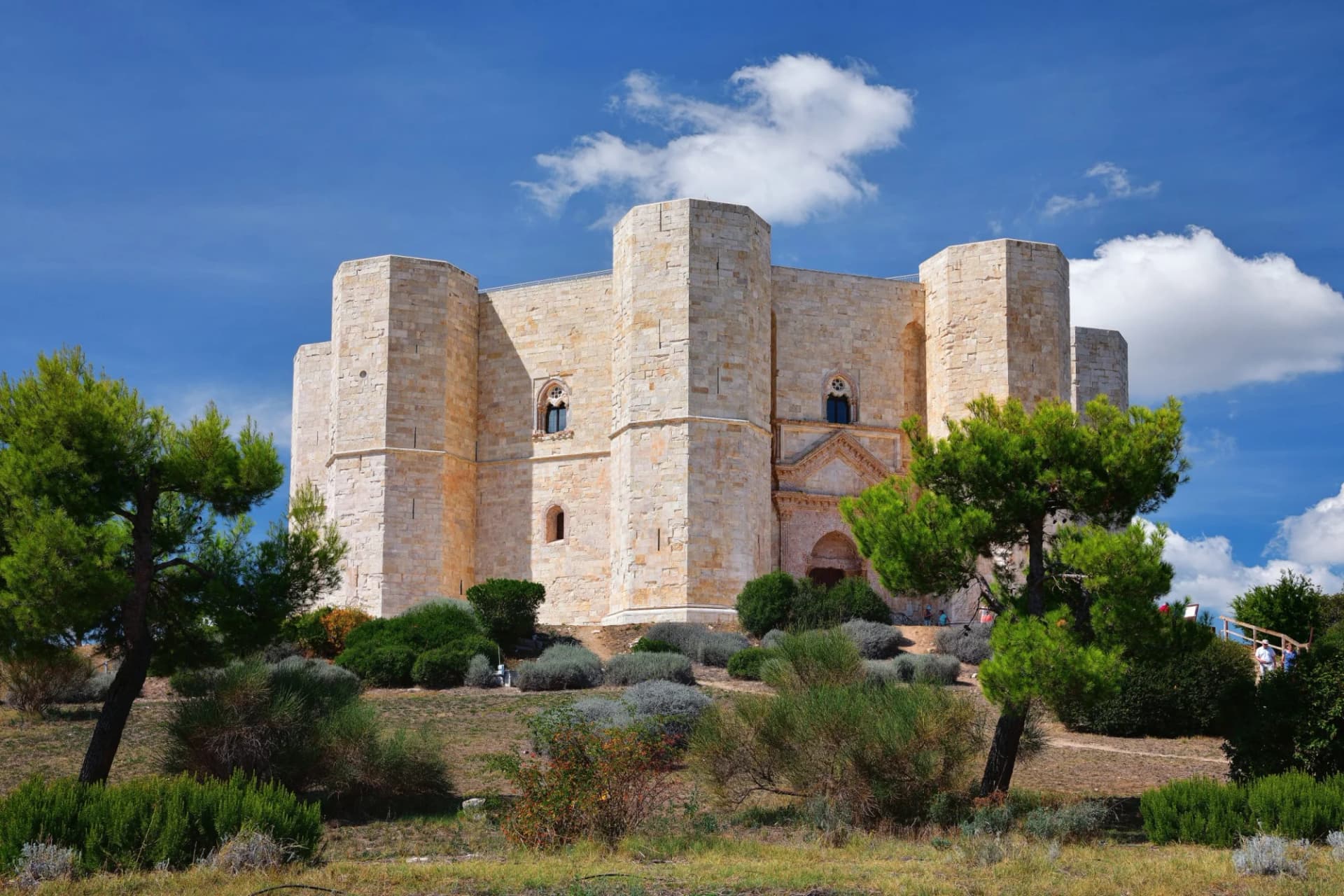 Castel del Monte fortress on a sunny day with green trees and blue sky with clouds