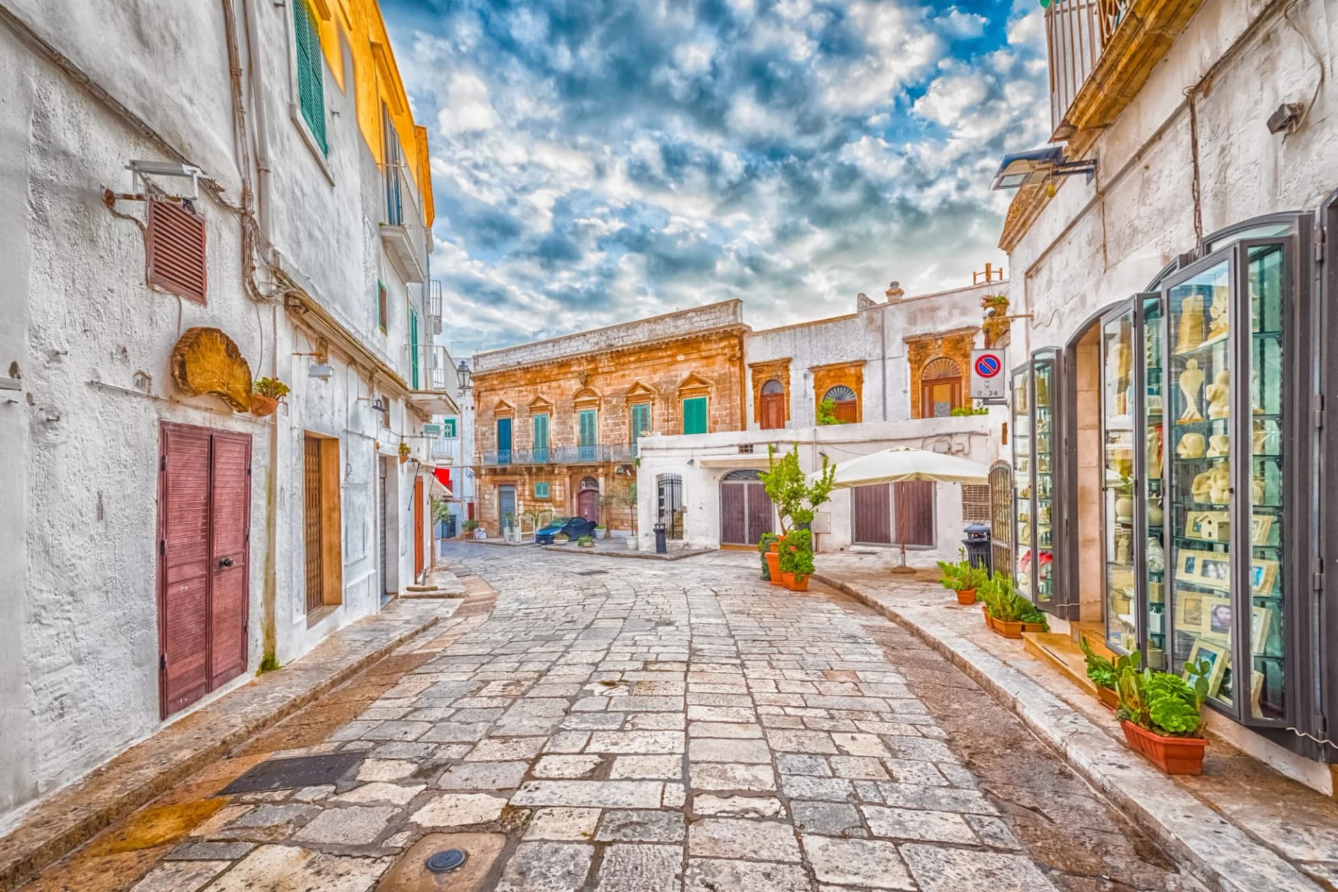 Cobblestone alleyway in Ostuni, Puglia, Italy, with white buildings and cloudy sky.