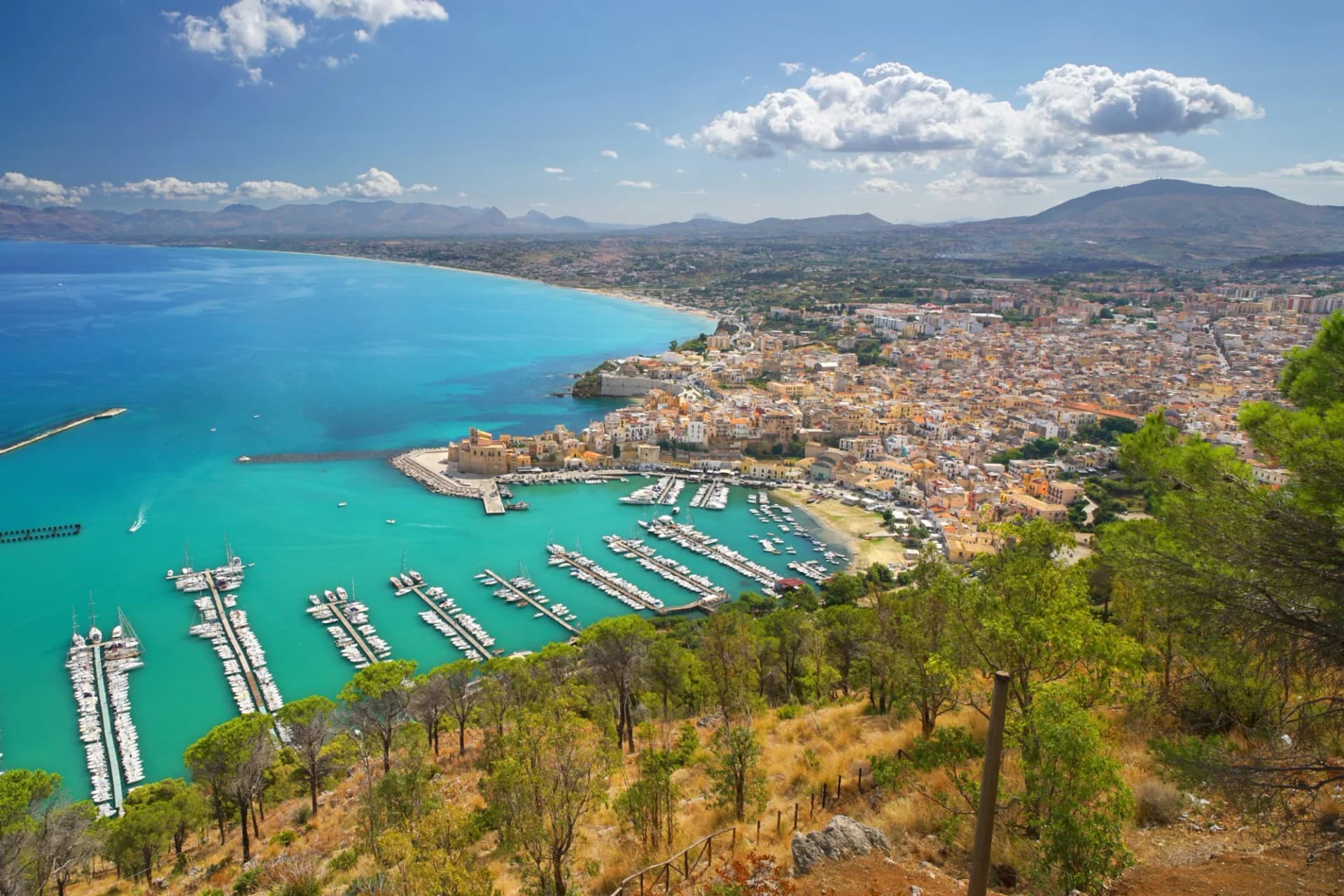 View of Castellammare del Golfo harbor, town, and turquoise sea from a hillside.