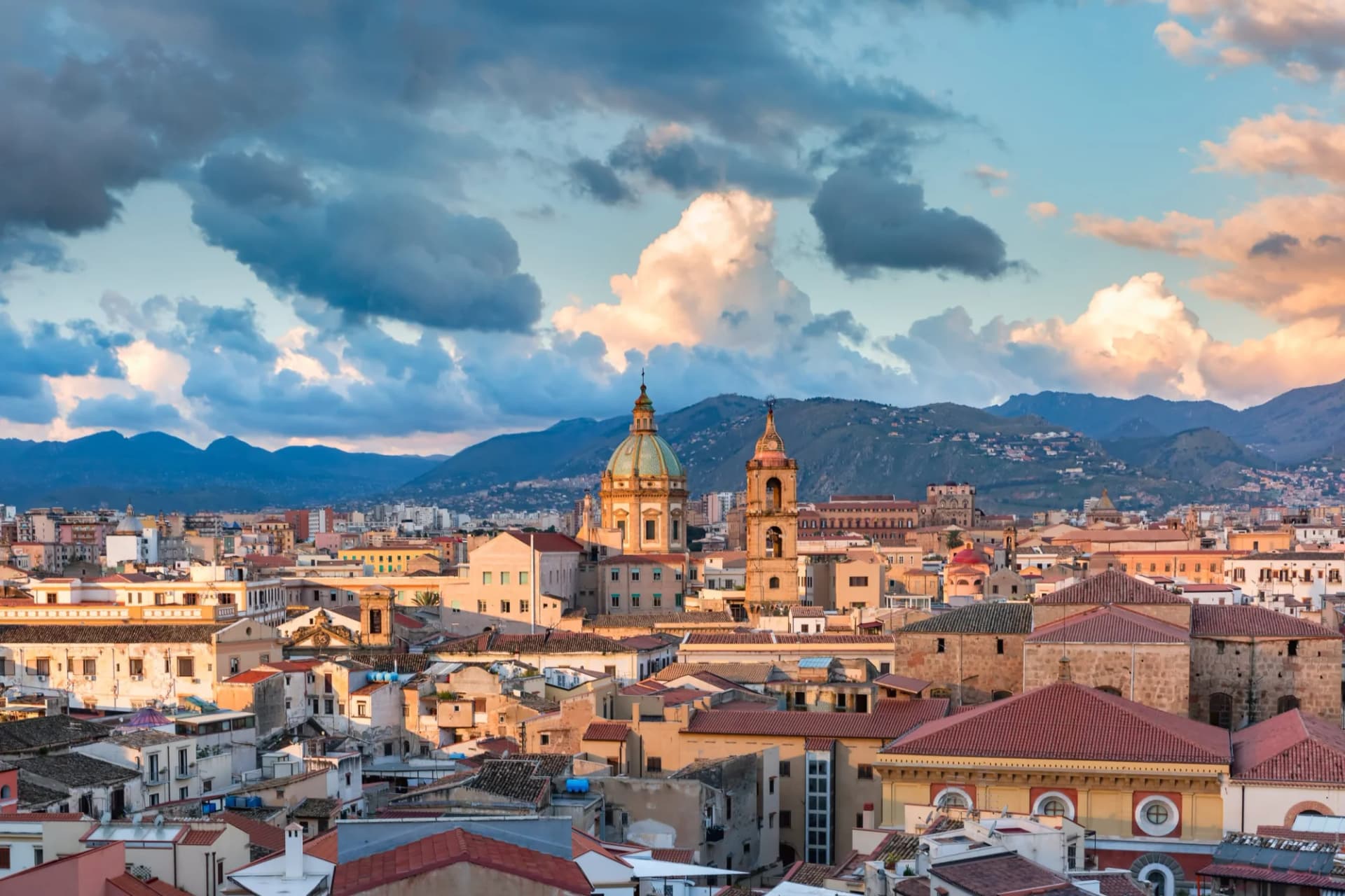 Palermo cityscape with historic domes and terracotta roofs against mountains at sunset, Sicily, Italy.