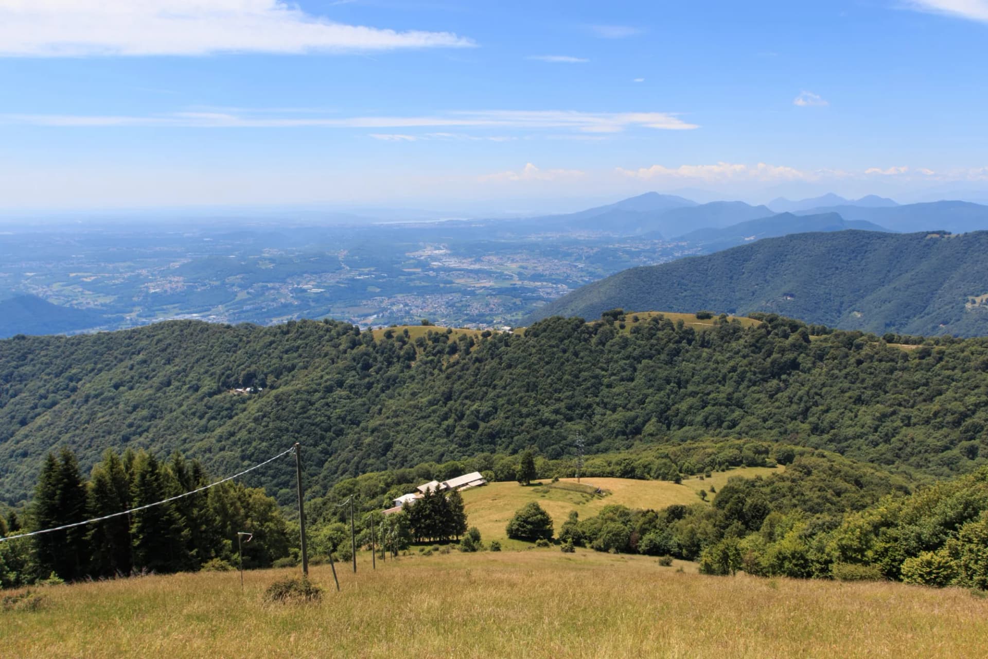 Mountain landscape view over forested hills toward a hazy valley city and distant blue mountains.