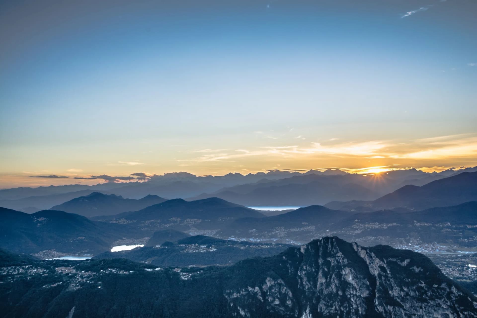 Mountain ranges at sunset over valleys with lakes and scattered town lights.