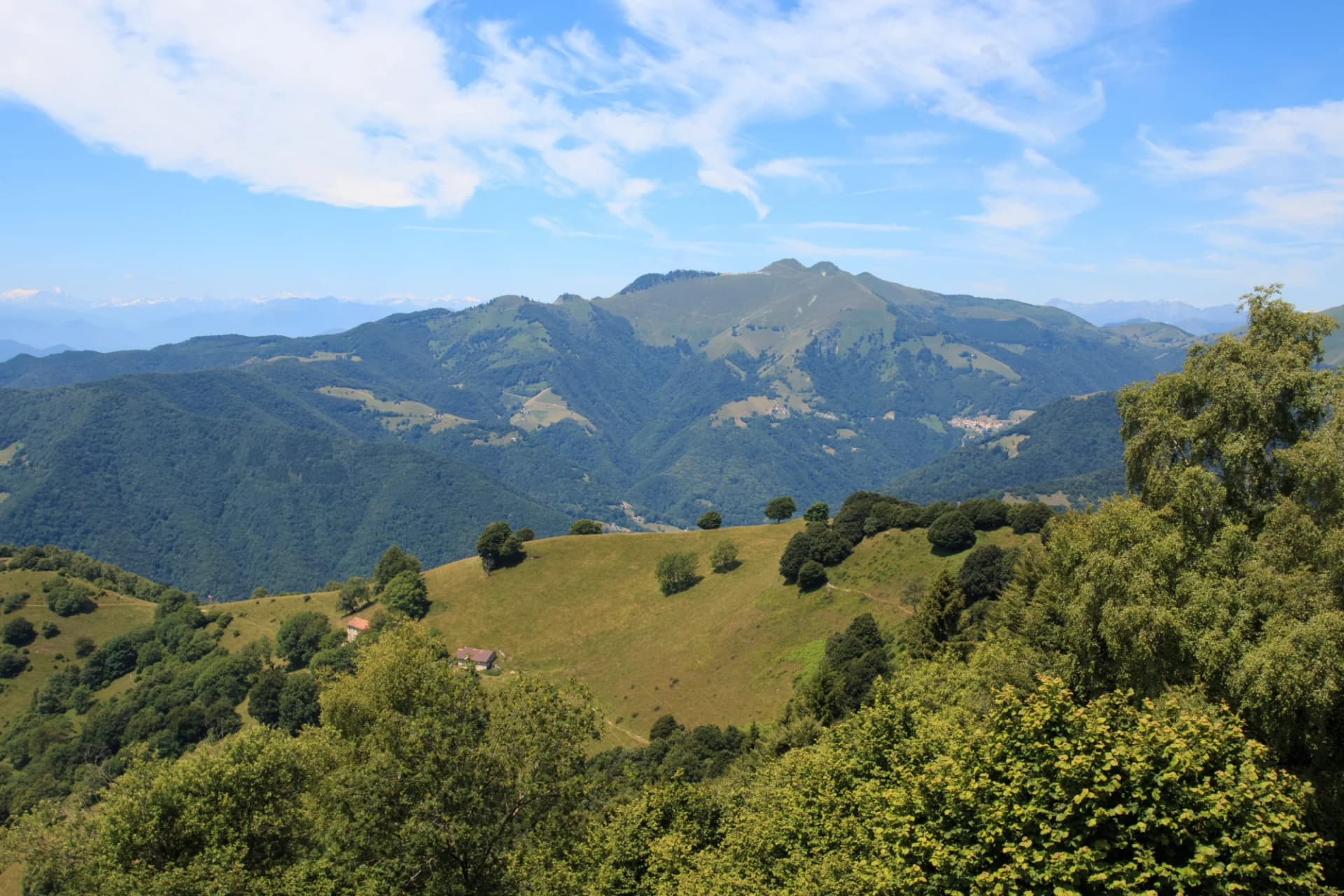 Rolling green mountains under a blue sky with white clouds, featuring a small house on a grassy slope.