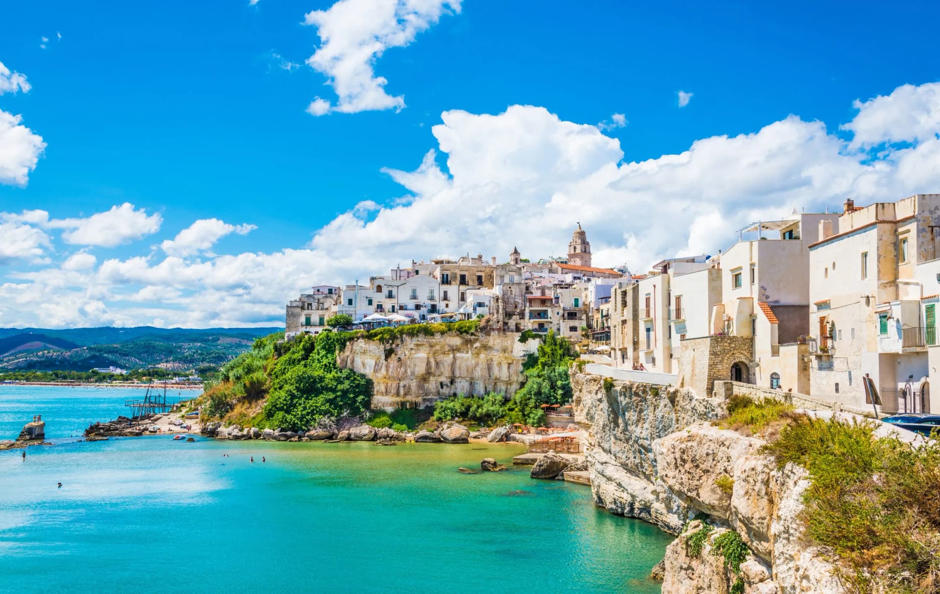 White buildings atop cliffs overlooking turquoise water in Apulia, Italy.