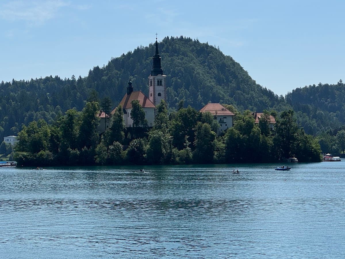 Church on island in Lake Bled with forested hill background and boats on water