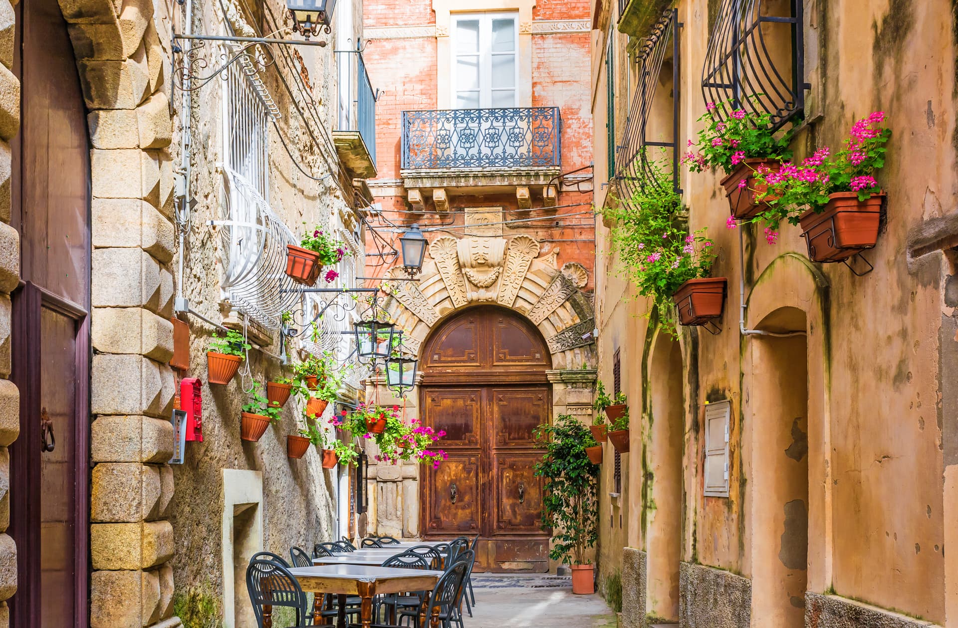 Outdoor dining tables on narrow Italian street with flower boxes and ornate doorway