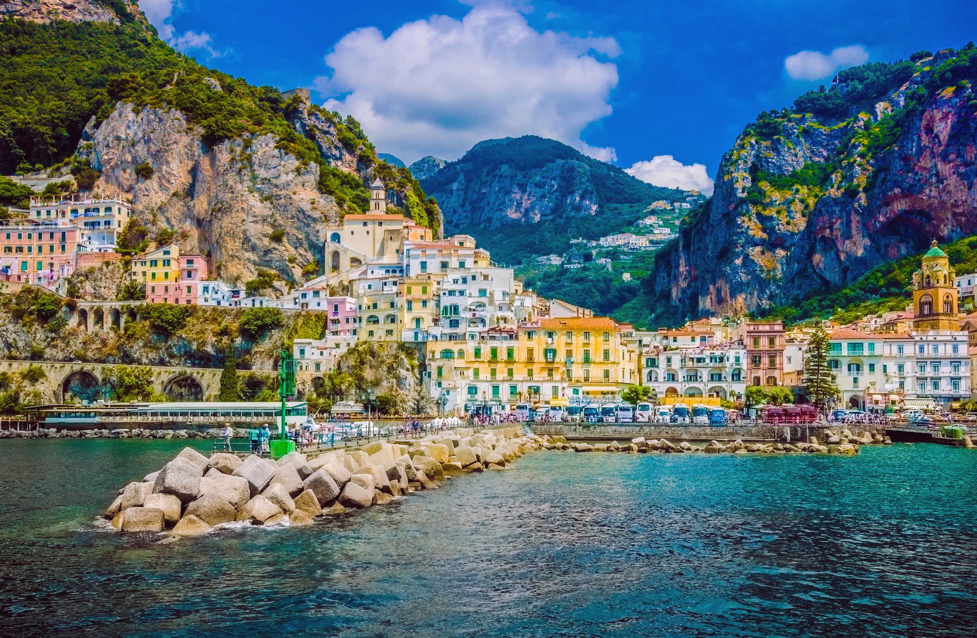 Coastal town with colorful buildings built into steep green mountainsides, viewed from the sea.