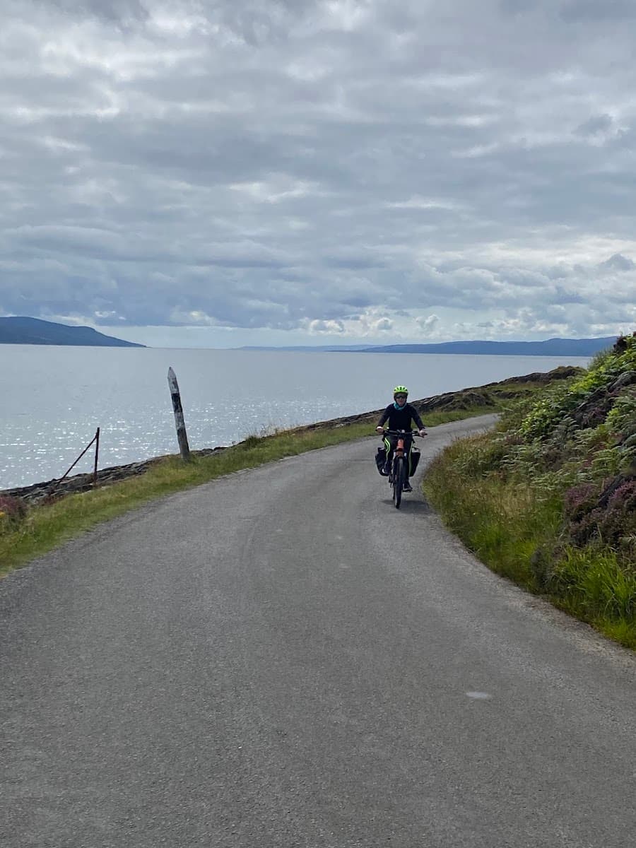 Cyclist riding a bicycle on a coastal road next to the sea under a cloudy sky
