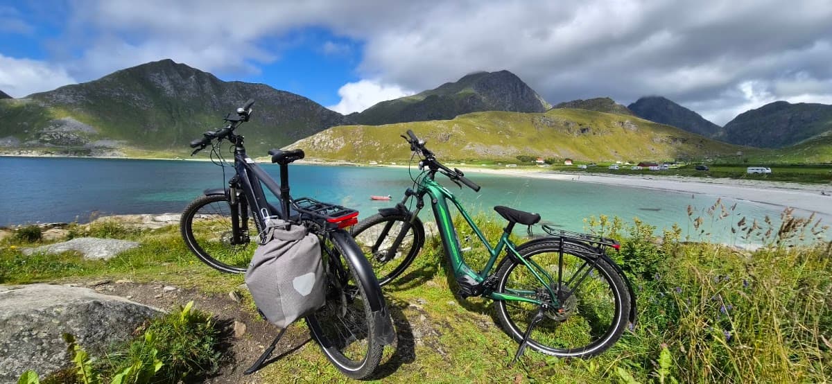 Two bicycles parked on grassy coastal hill overlooking turquoise beach and mountains